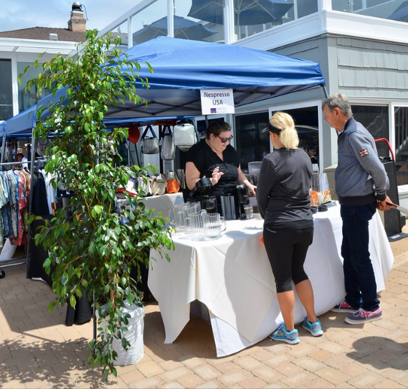 People browsing a white-tablecloth stall under a blue canopy at an outdoor market