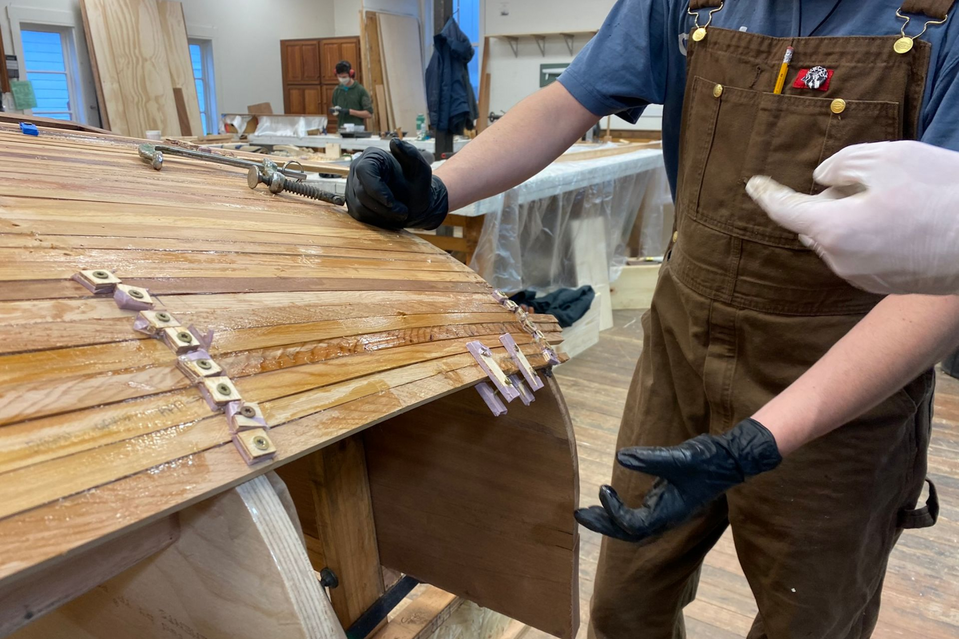 Worker in brown overalls handles varnished wooden panels in a workshop.