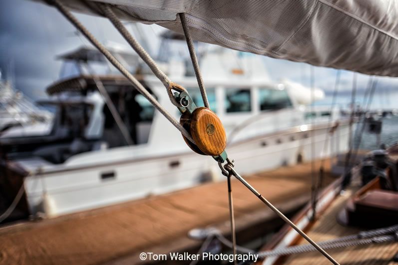 Orange sailing pulley and rope on a yacht deck with blurred boats in the marina background
