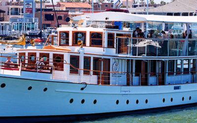 White passenger boat with wooden trim docked at a marina, with people visible on the deck