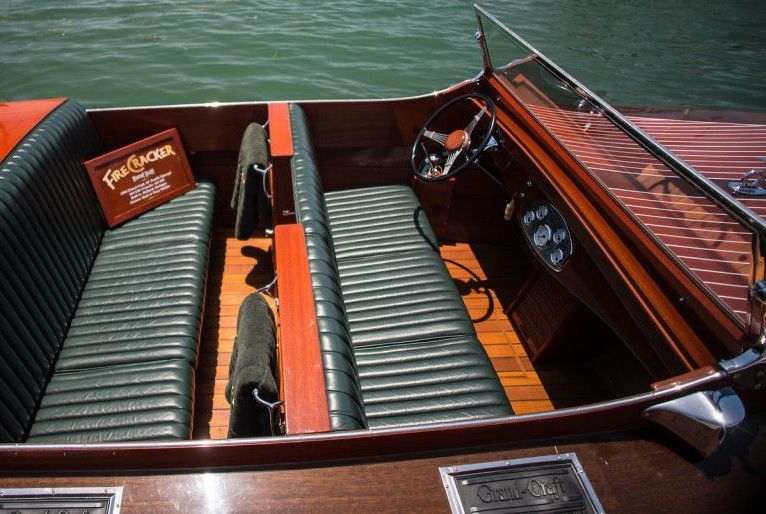 Wooden boat interior with green bench seats and steering wheel on the water