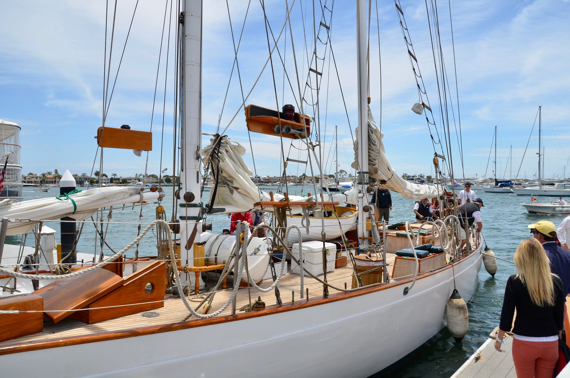 White sailboat docked at a marina with people on deck under a bright blue sky
