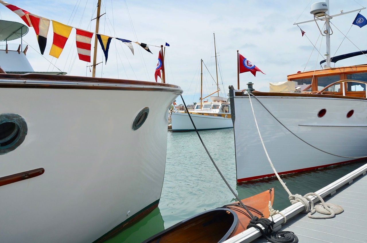 Two docked sailboats with colorful flags on calm water under a clear sky.