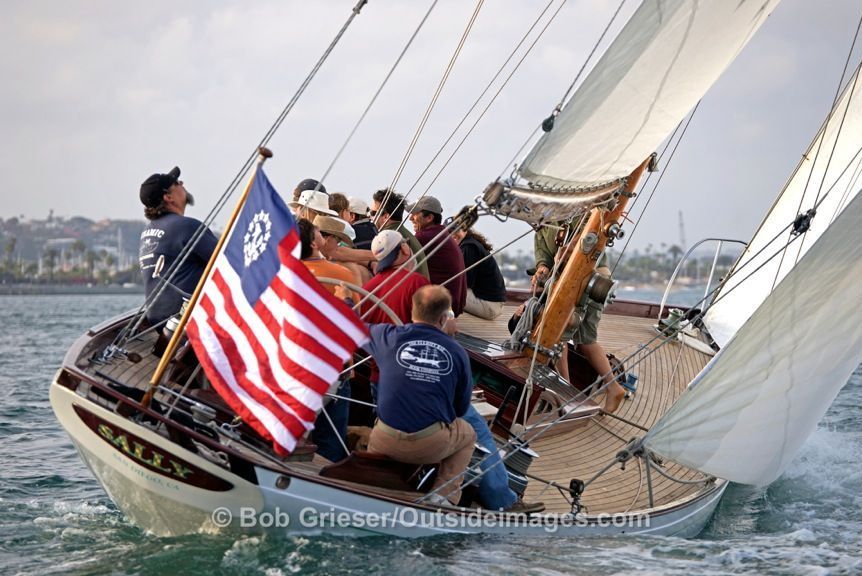 Sailboat crew racing on choppy water, raising a red, white and blue flag under full sails