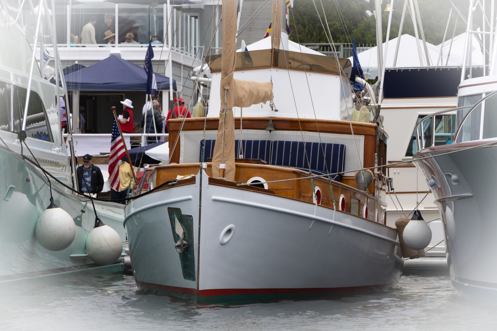 Two docked motorboats in a marina, with people onboard and white fenders hanging over the sides.
