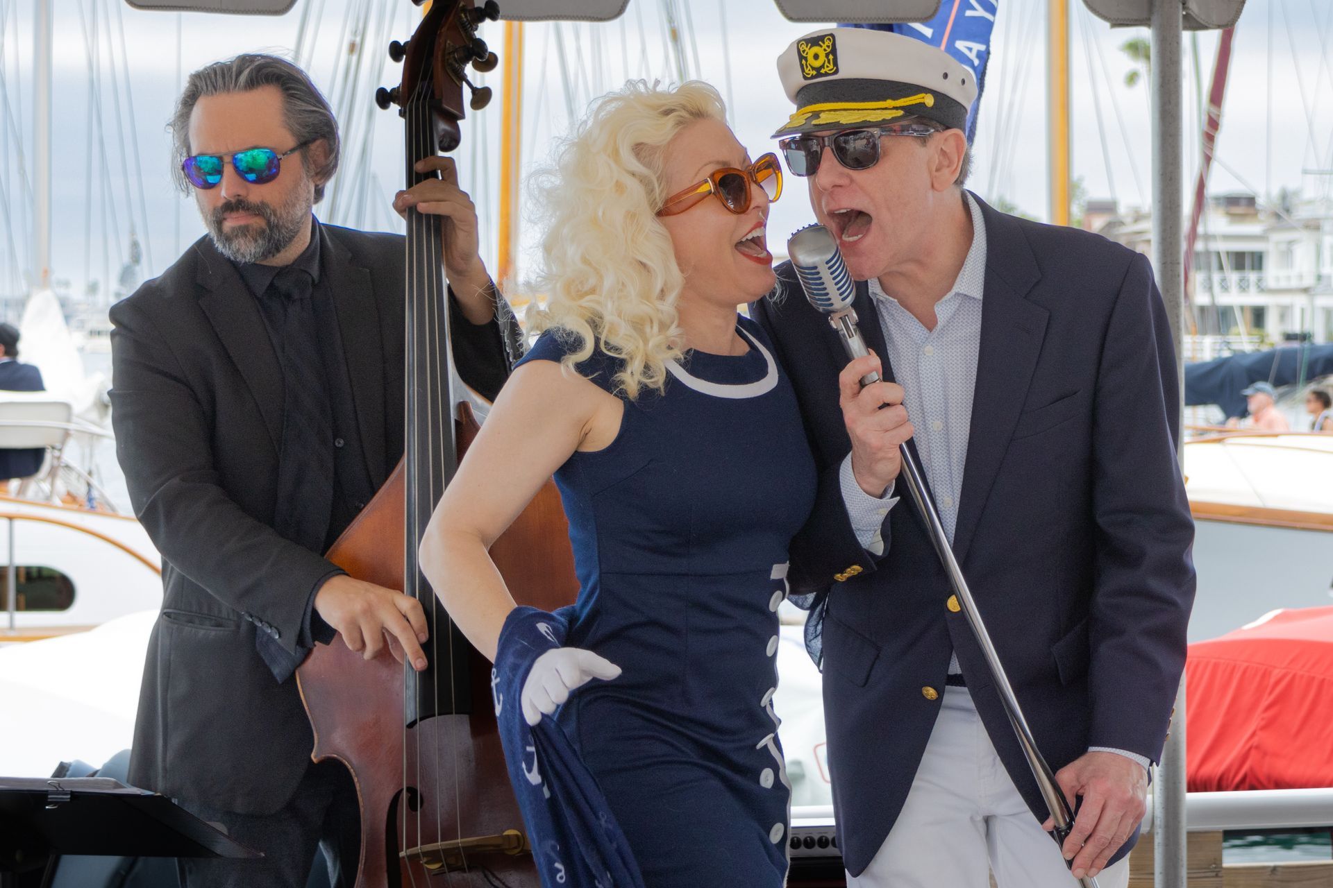 Three musicians perform on a sailboat, with a singer at a microphone and a bassist behind her.