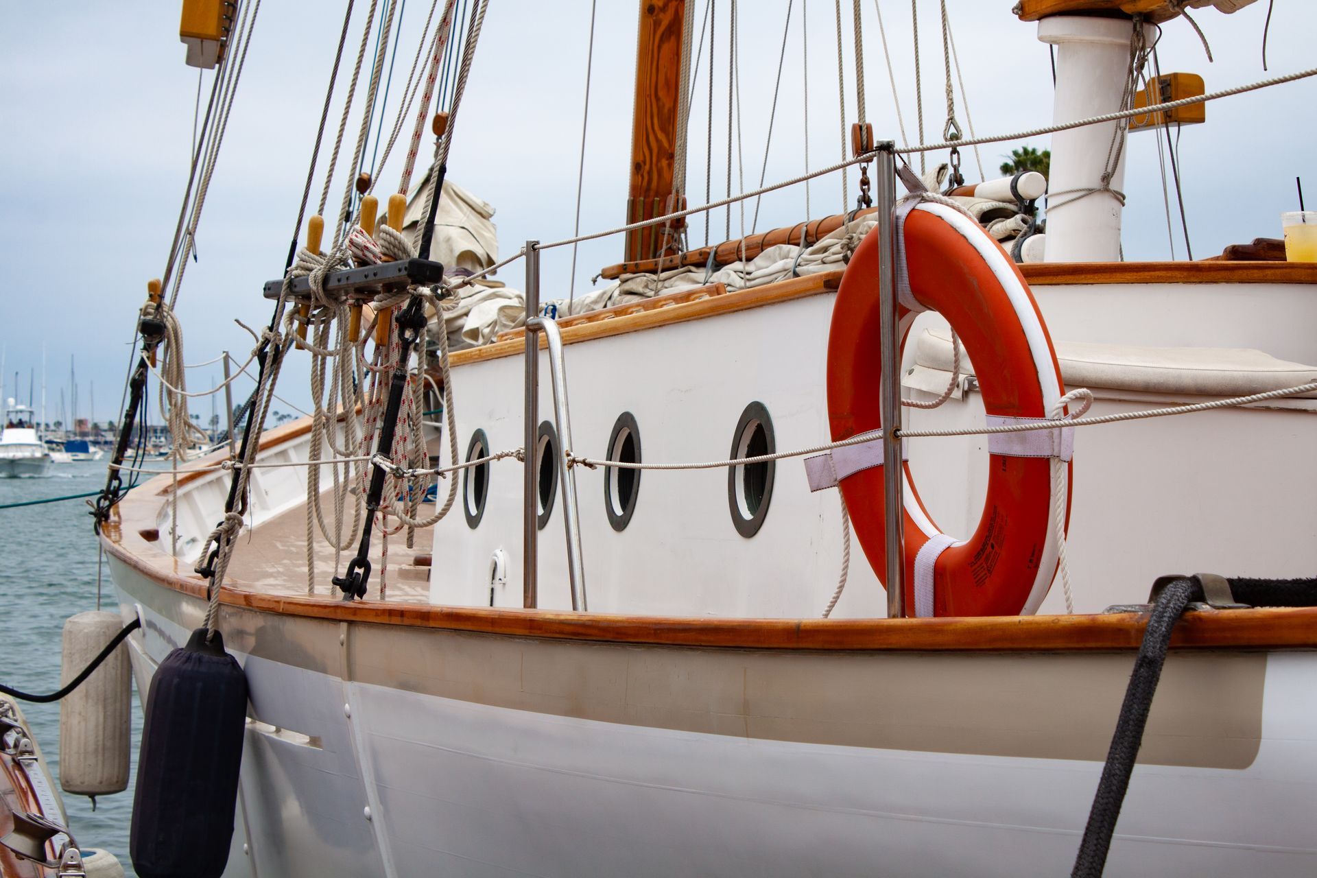 Docked white sailboat with red life preserver and wooden mast by the harbor