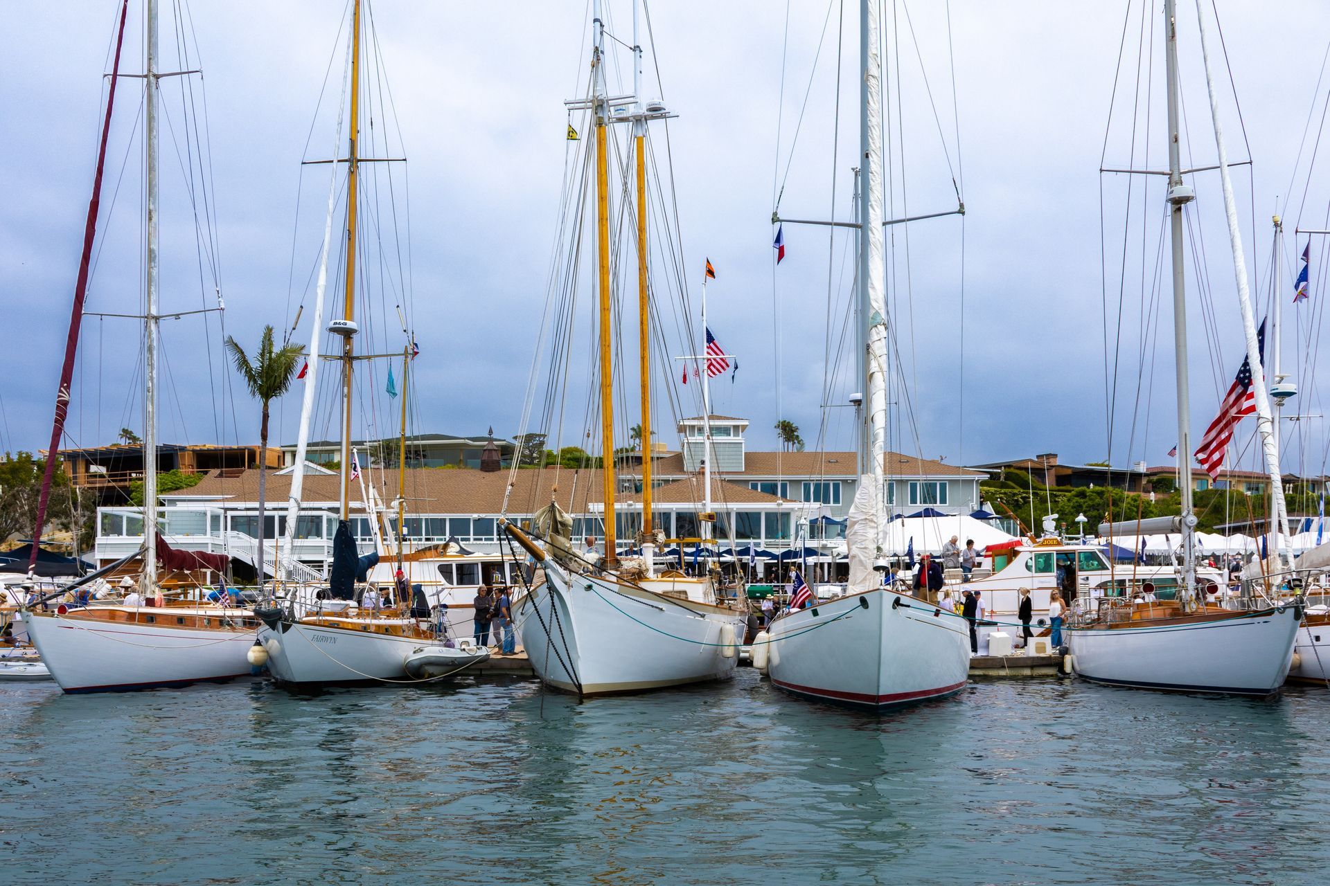 Sailboats and yachts docked at a marina on calm water under a cloudy sky