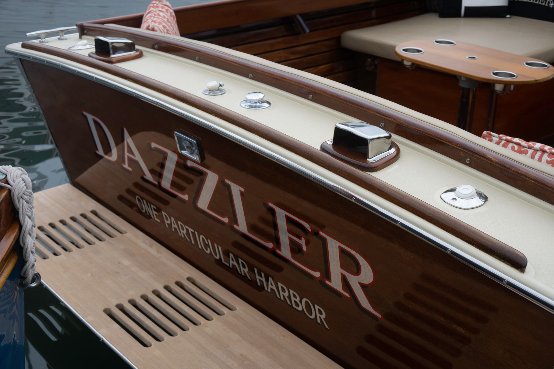 Wooden speedboat deck with polished trim and “Dazzler” painted on the hull, docked in a marina.