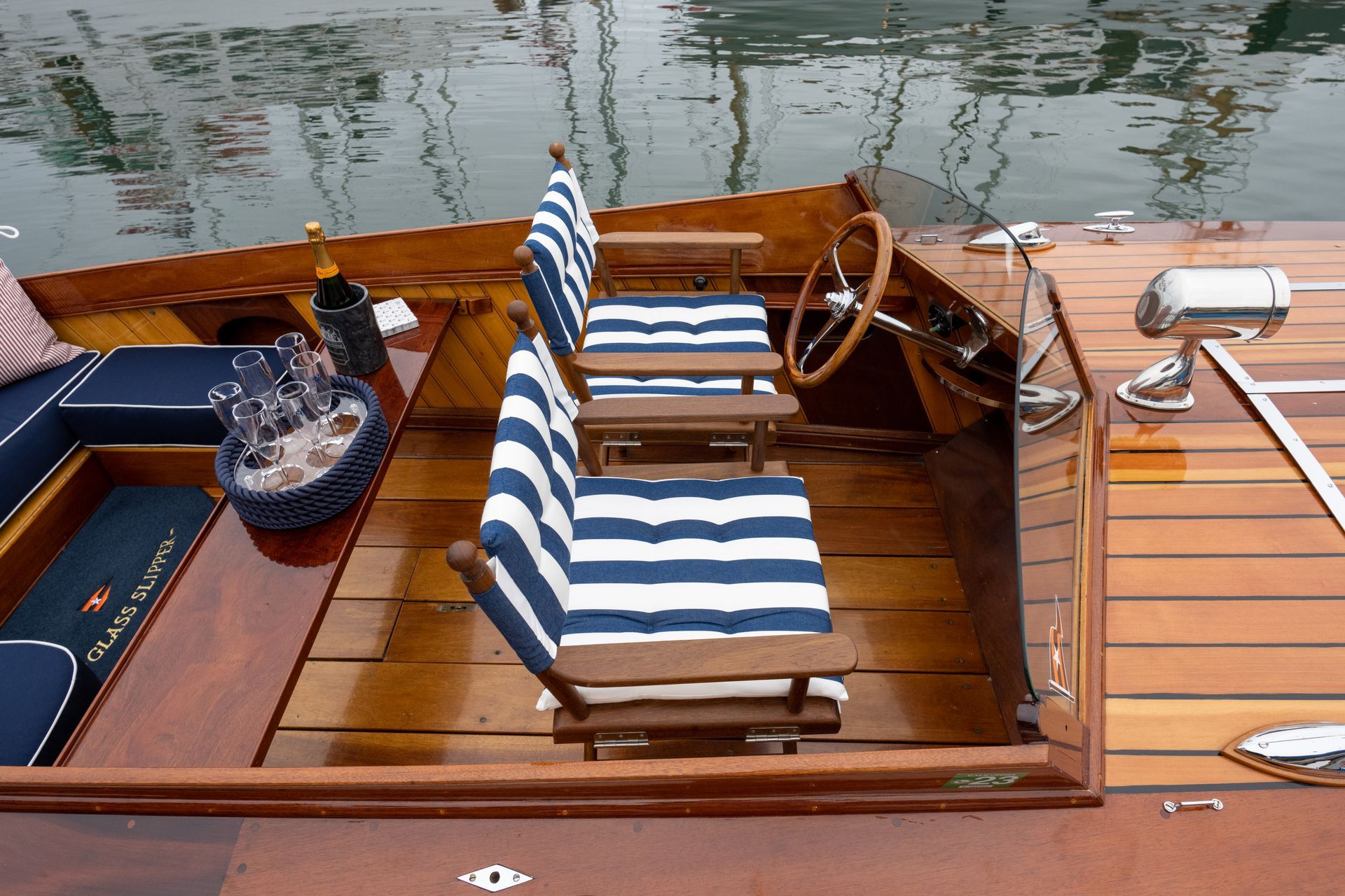 Striped-cushion wooden boat deck with steering wheel, cup holder, and water in the background