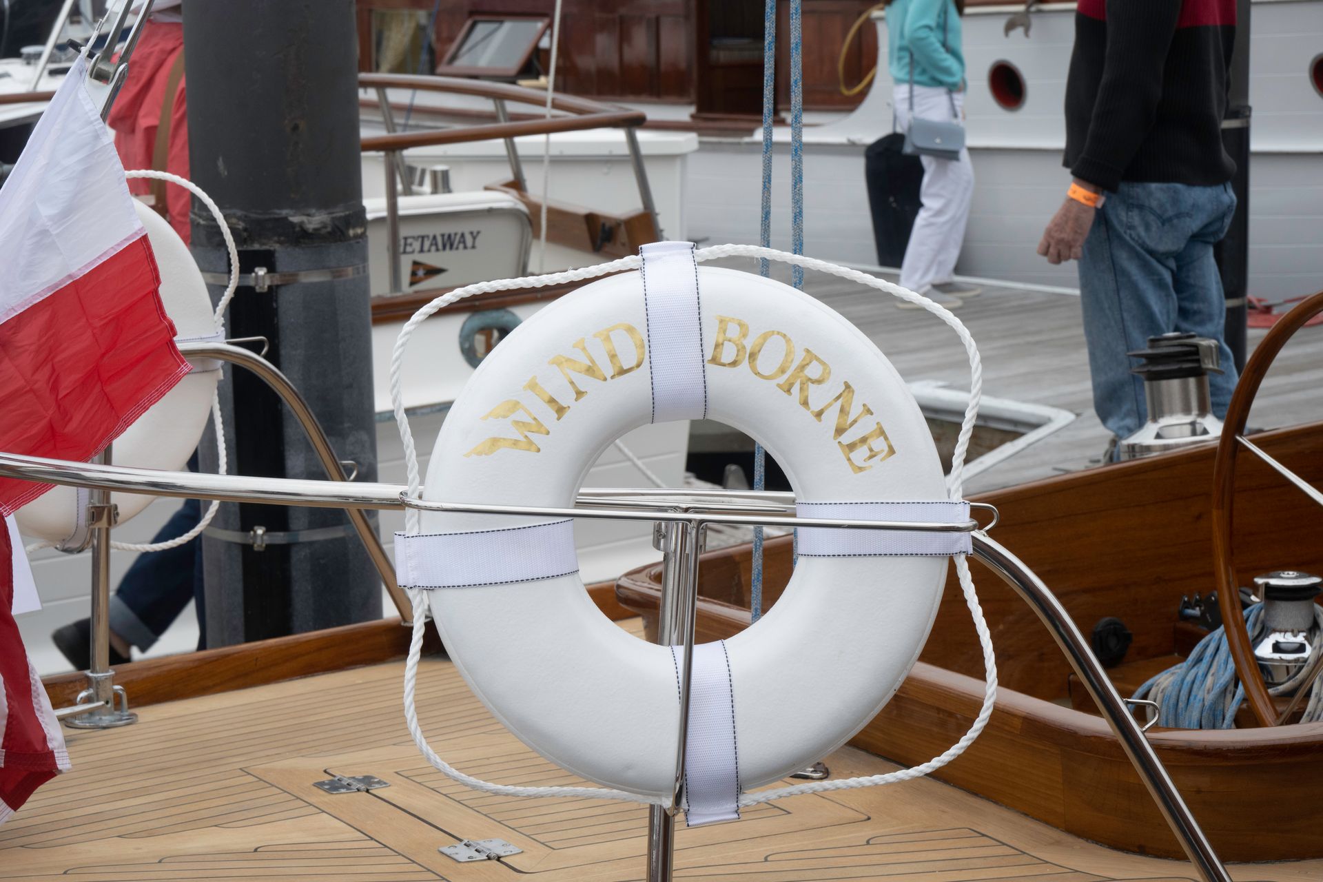 White life ring with gold lettering on a boat deck, beside ropes and a red flag