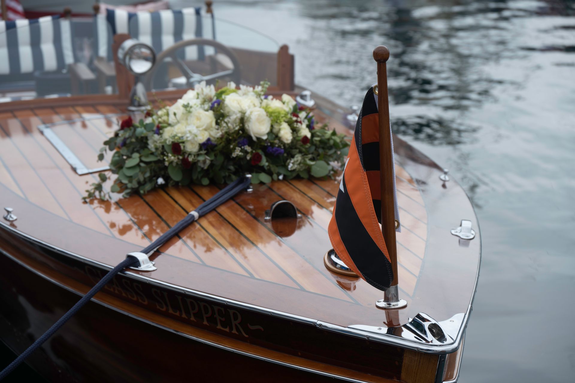 Wooden model boat with white flowers and orange sail floating on calm water