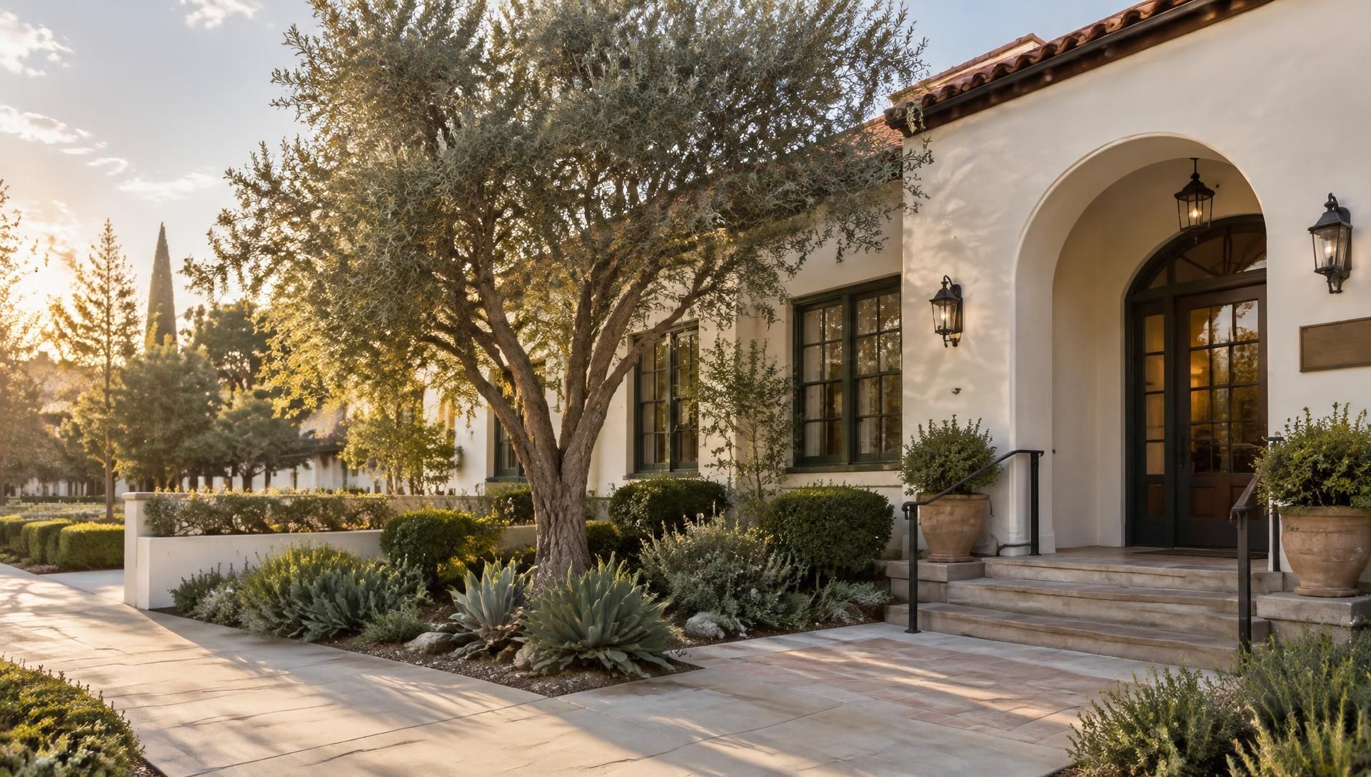 Spanish-style house exterior with arched entry, stone walkway, and desert landscaping at sunset