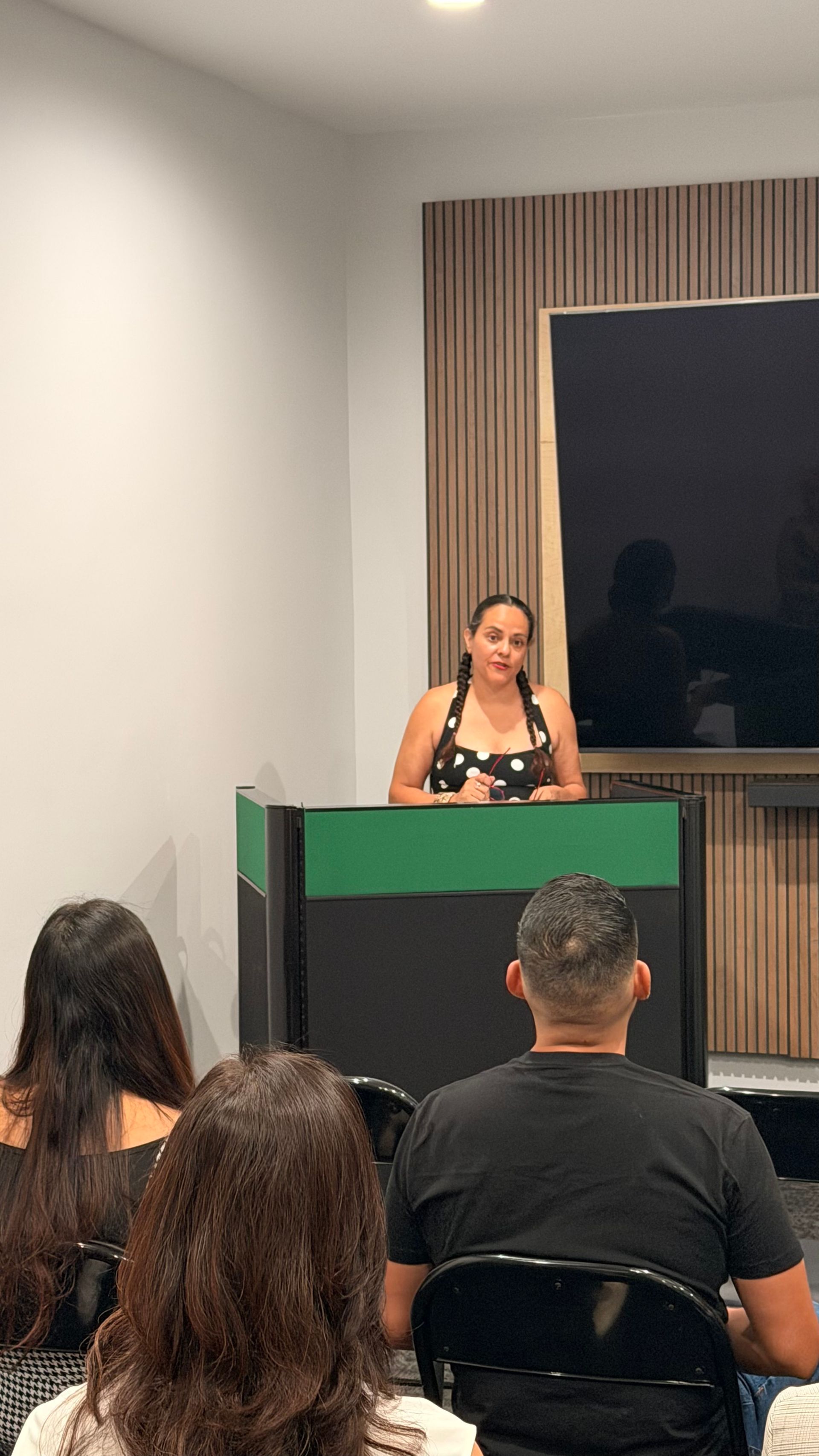 Speaker at a green podium addressing an audience in a modern conference room.
