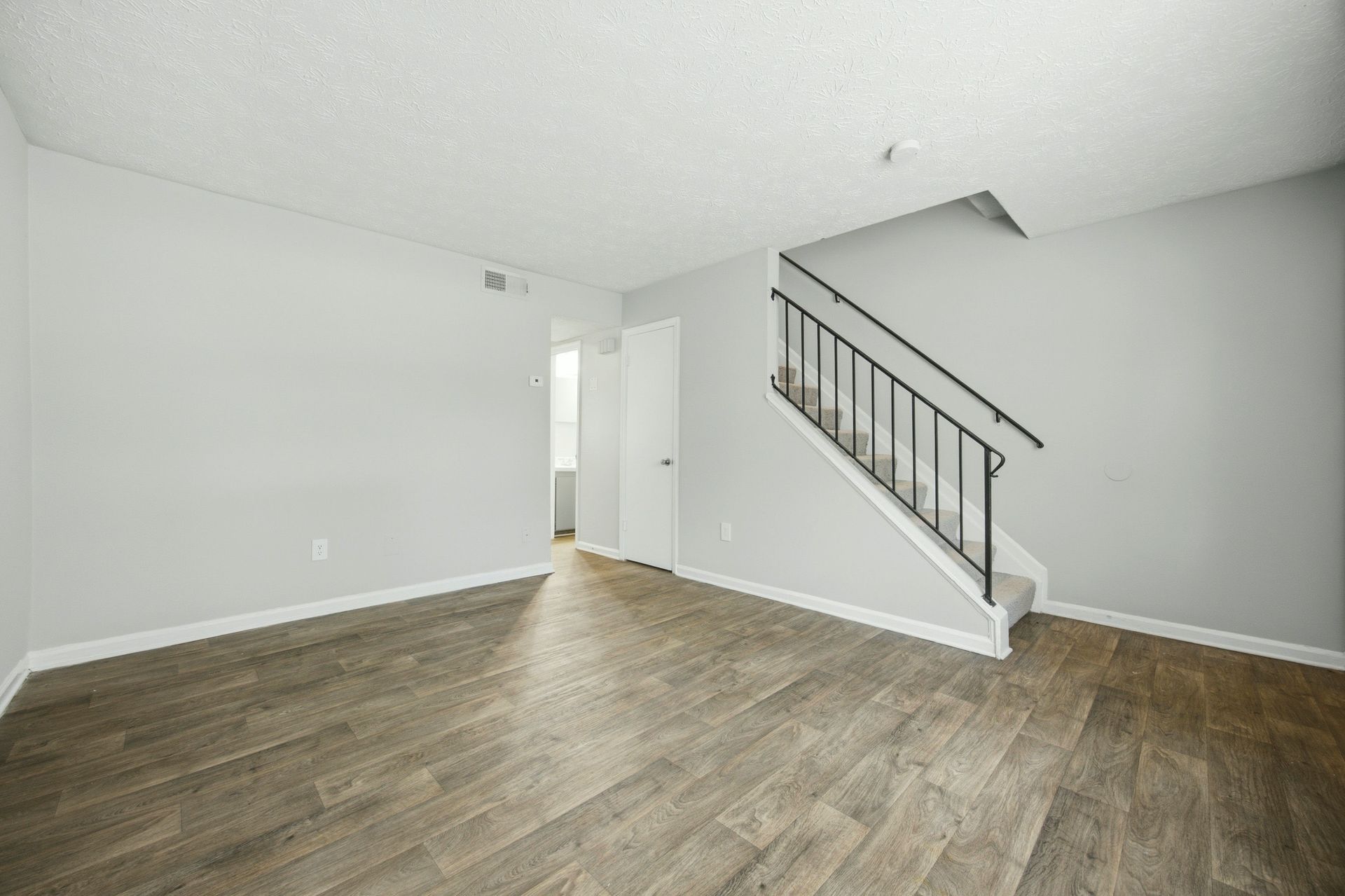 Empty living room with wood-look flooring, white walls, and a staircase on the right.