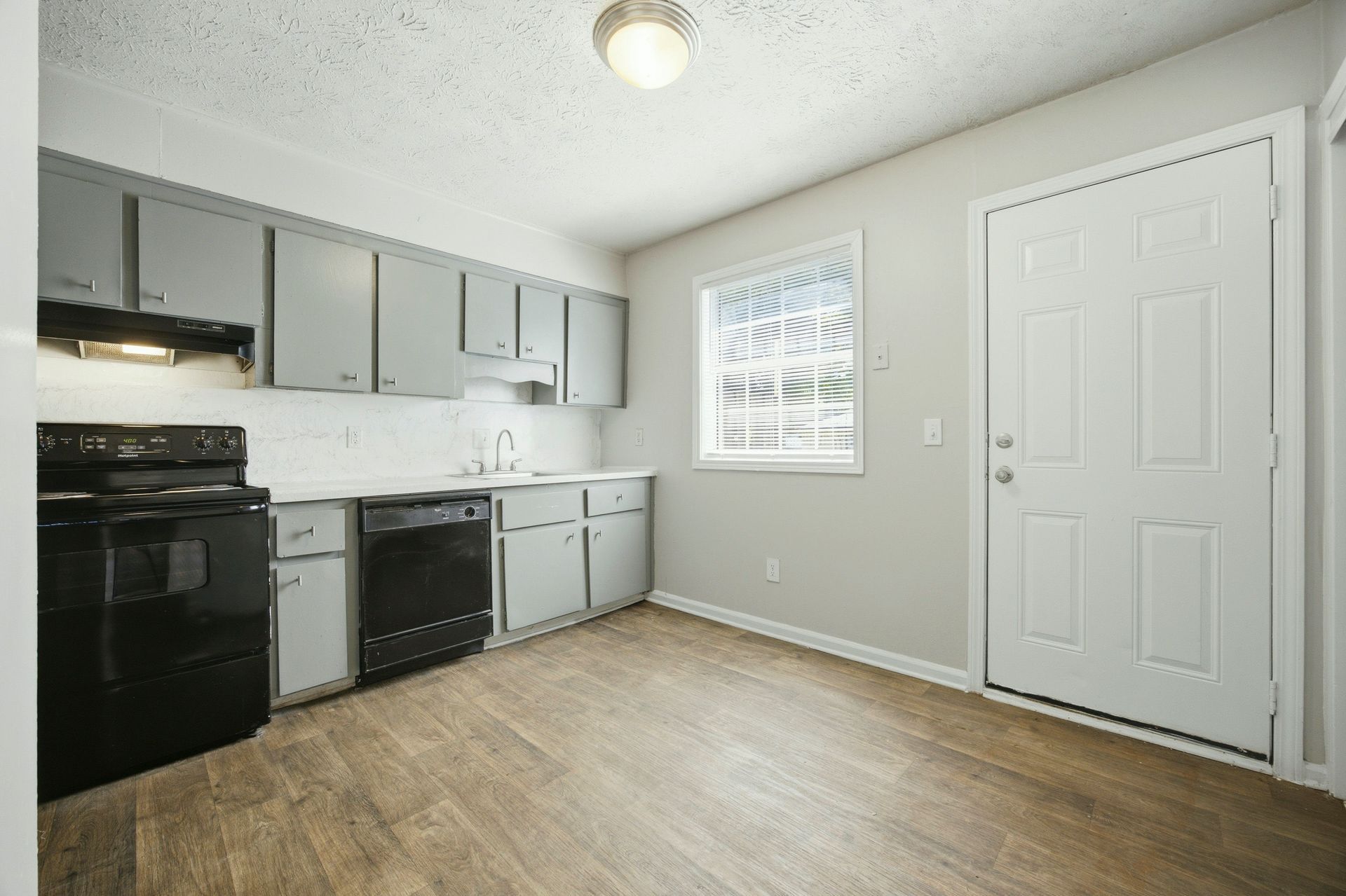 Small kitchen with gray cabinets, black appliances, white walls, and a door by a window.