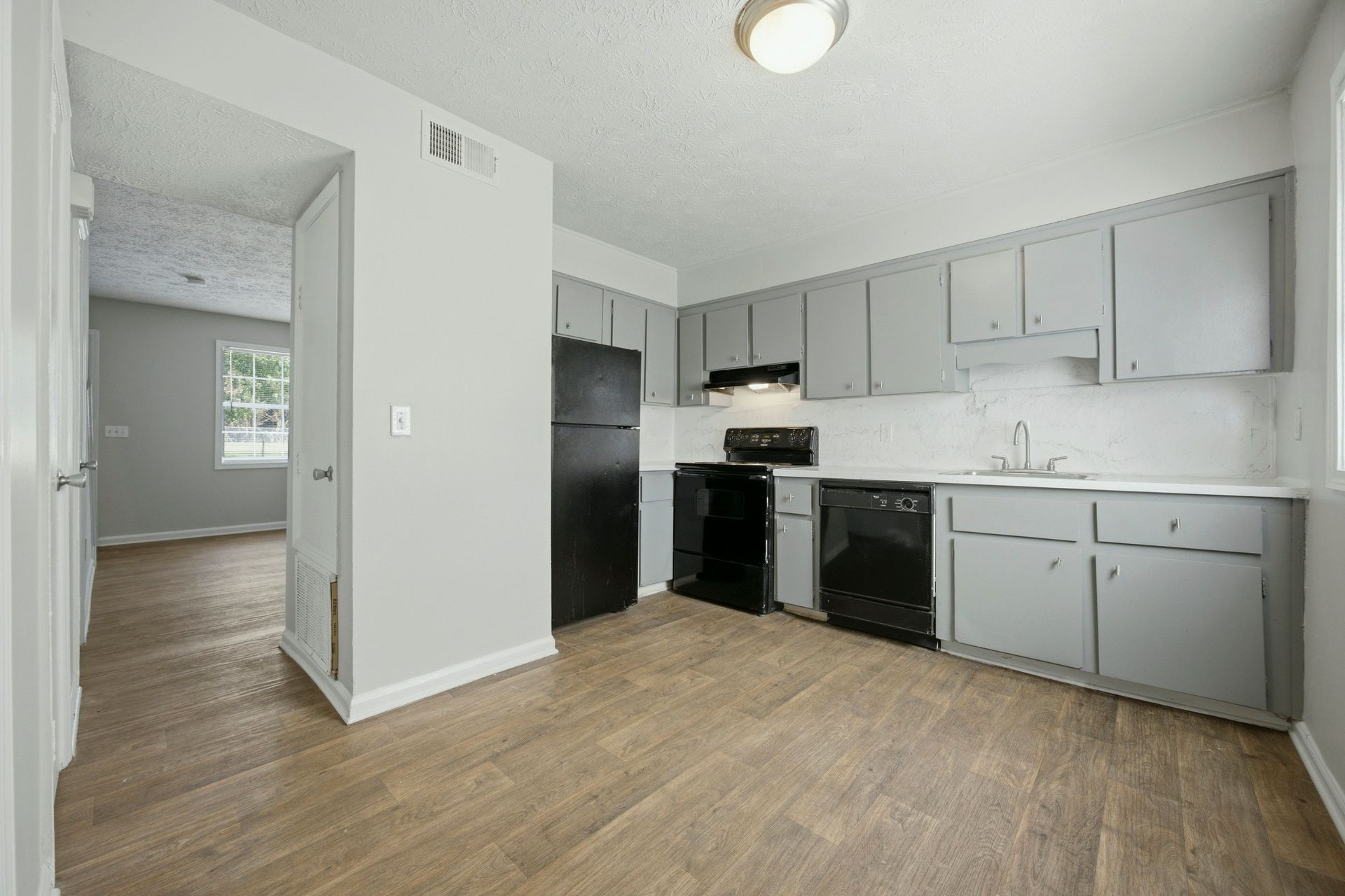 Empty modern kitchen with gray cabinets, black appliances, white countertops, and wood-look flooring