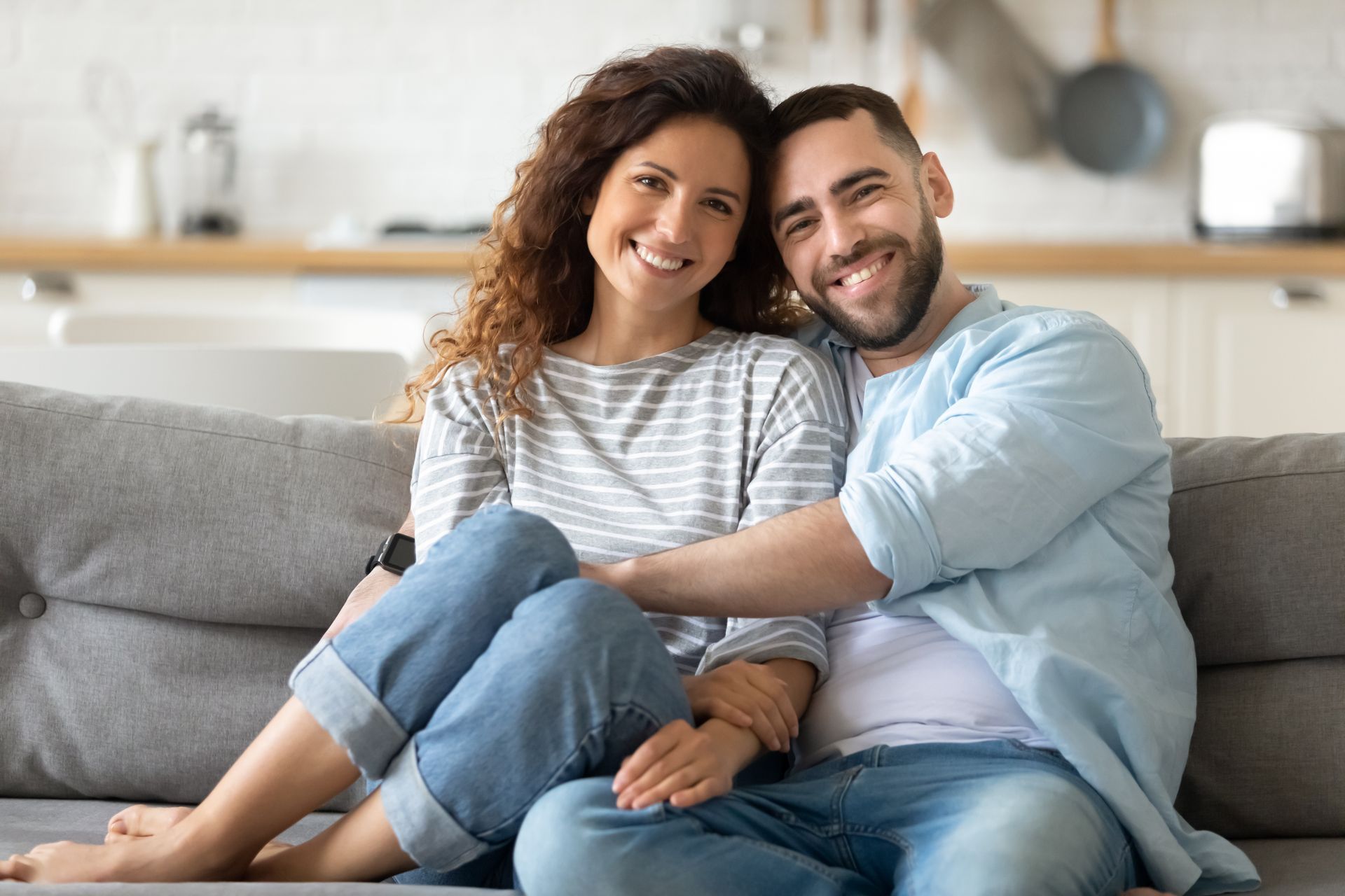 Couple smiling on a gray couch in a bright living room