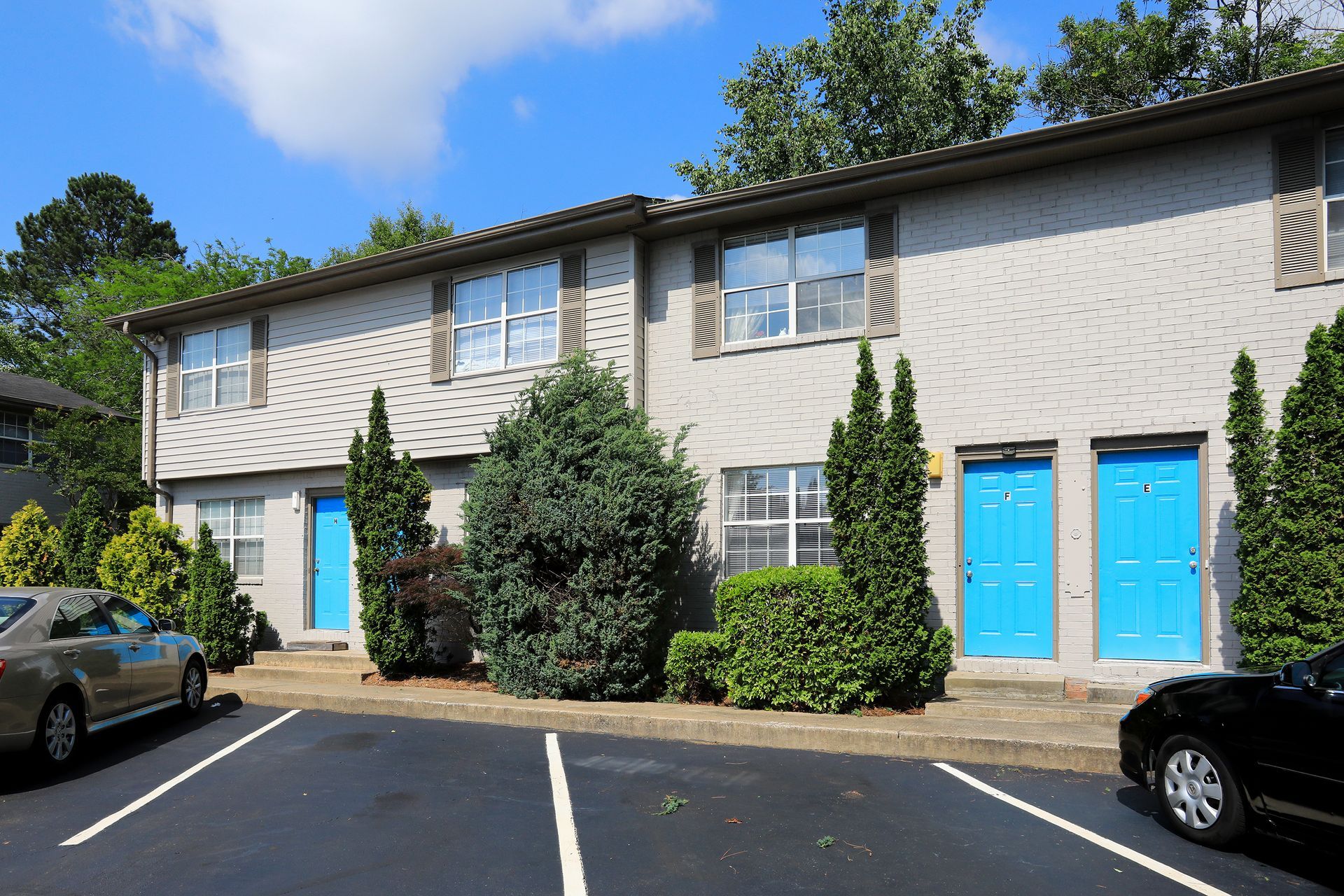 Two-story apartment building with blue doors and parked cars in a lot