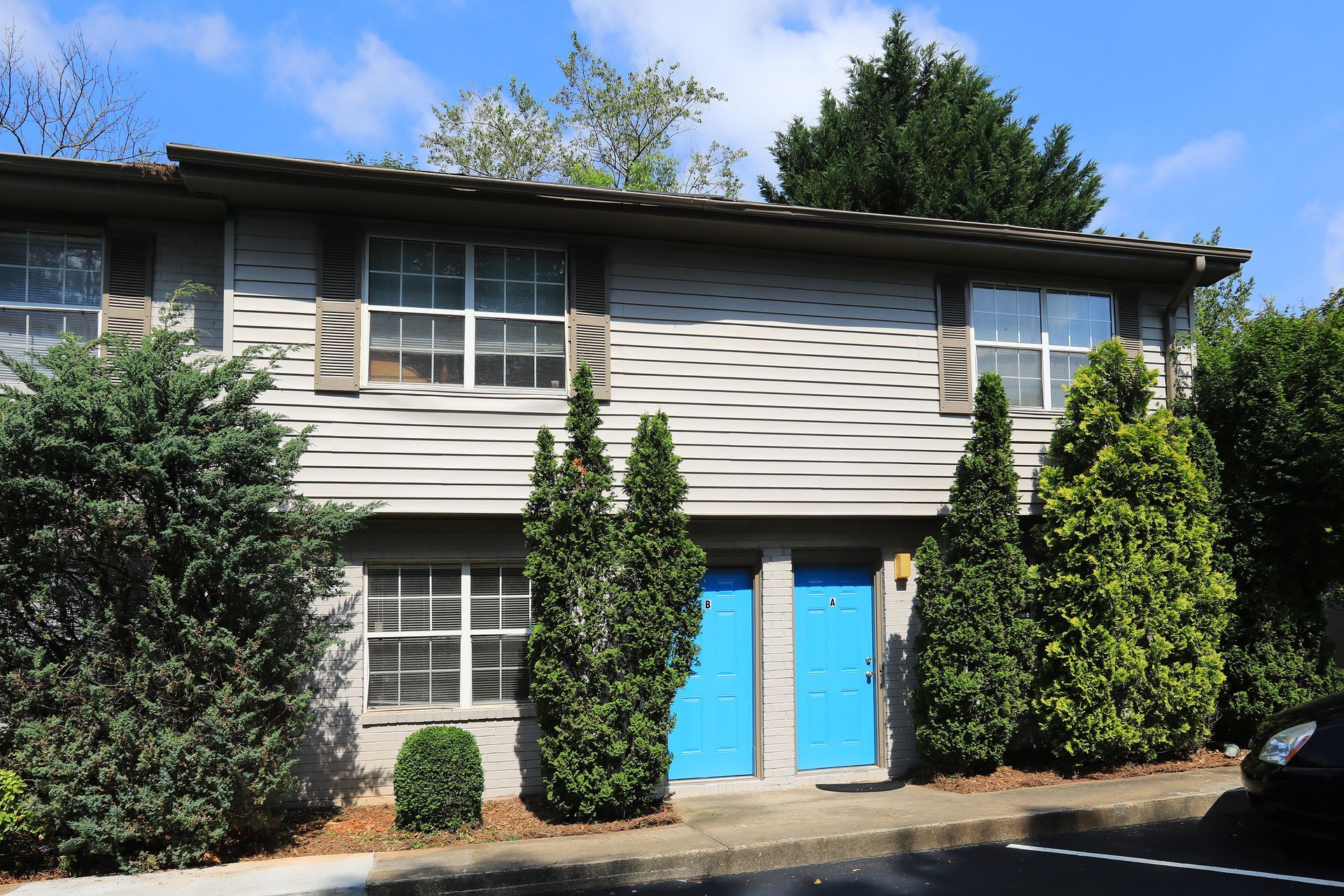 Two-story beige house with bright blue double doors, white windows, and shrubs in front