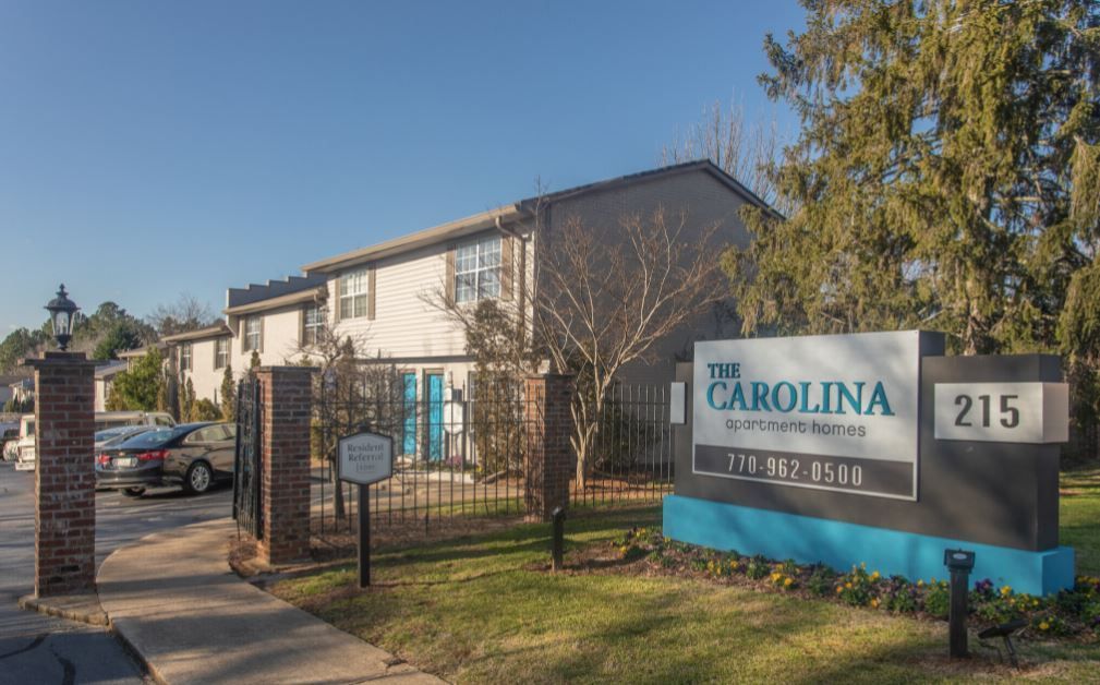 The Carolina building sign at 215, with apartment exterior and gate in sunlight.