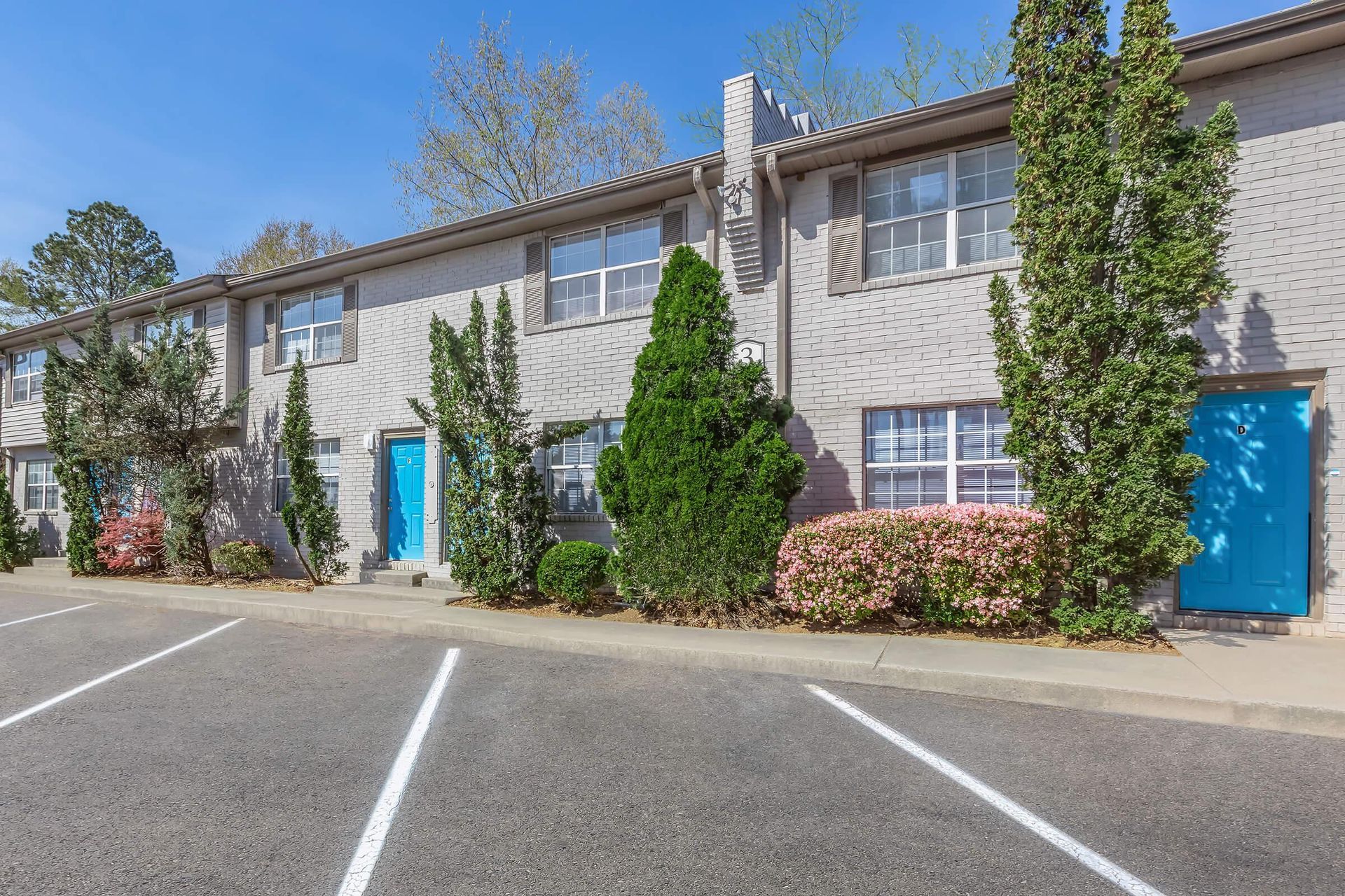 Apartment complex parking lot with blue doors and shrubs along the building