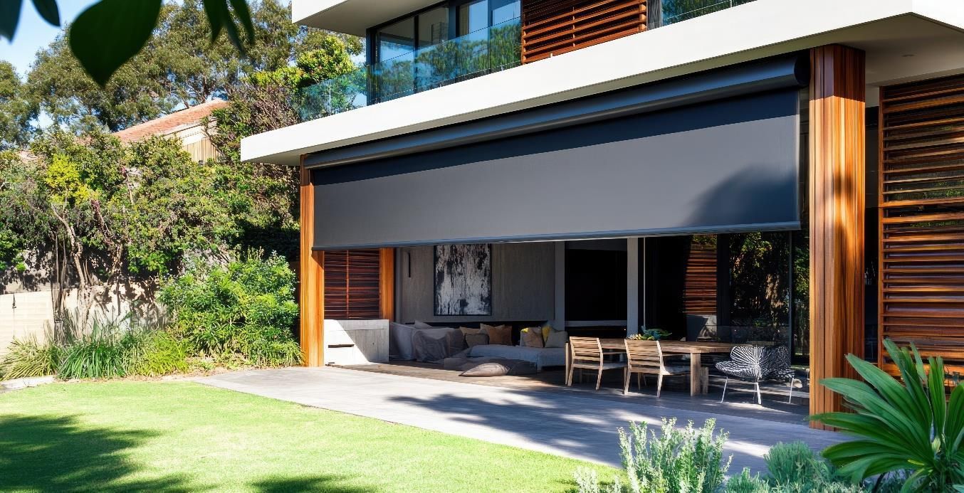 Modern house patio with a rolled-down outdoor shade, wooden facade, and garden lawn.