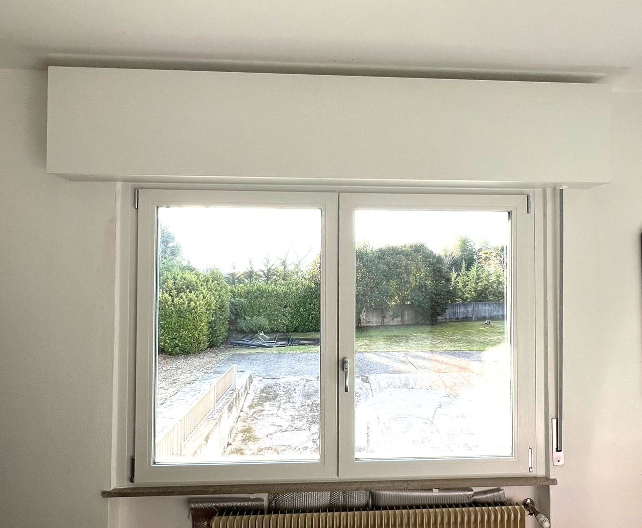 Una finestra bianca con una cornice bianca si trova in una stanza con un termosifone.