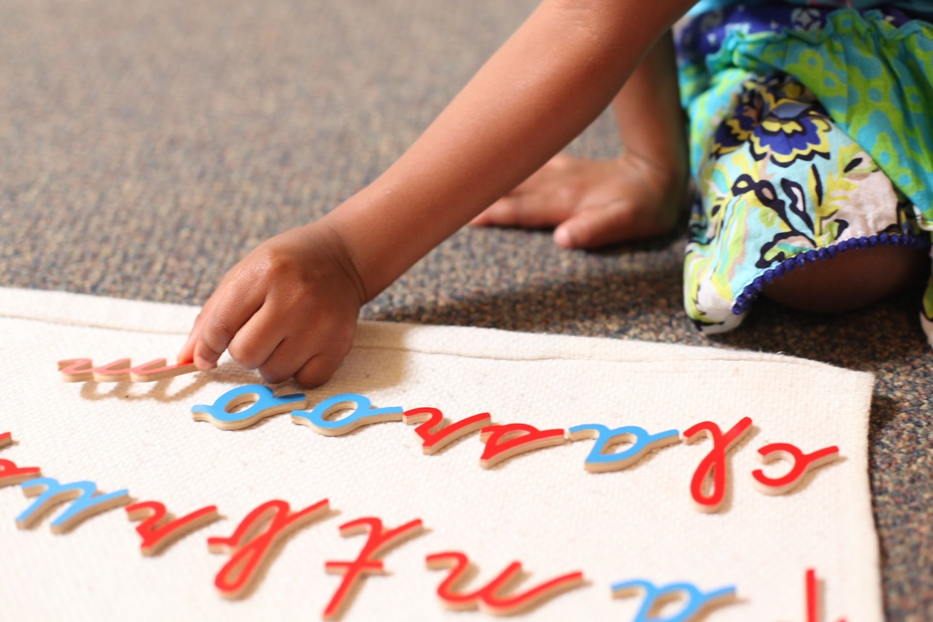 Child’s hand arranging colorful foam letters on a mat, with scattered letters and bare feet nearby