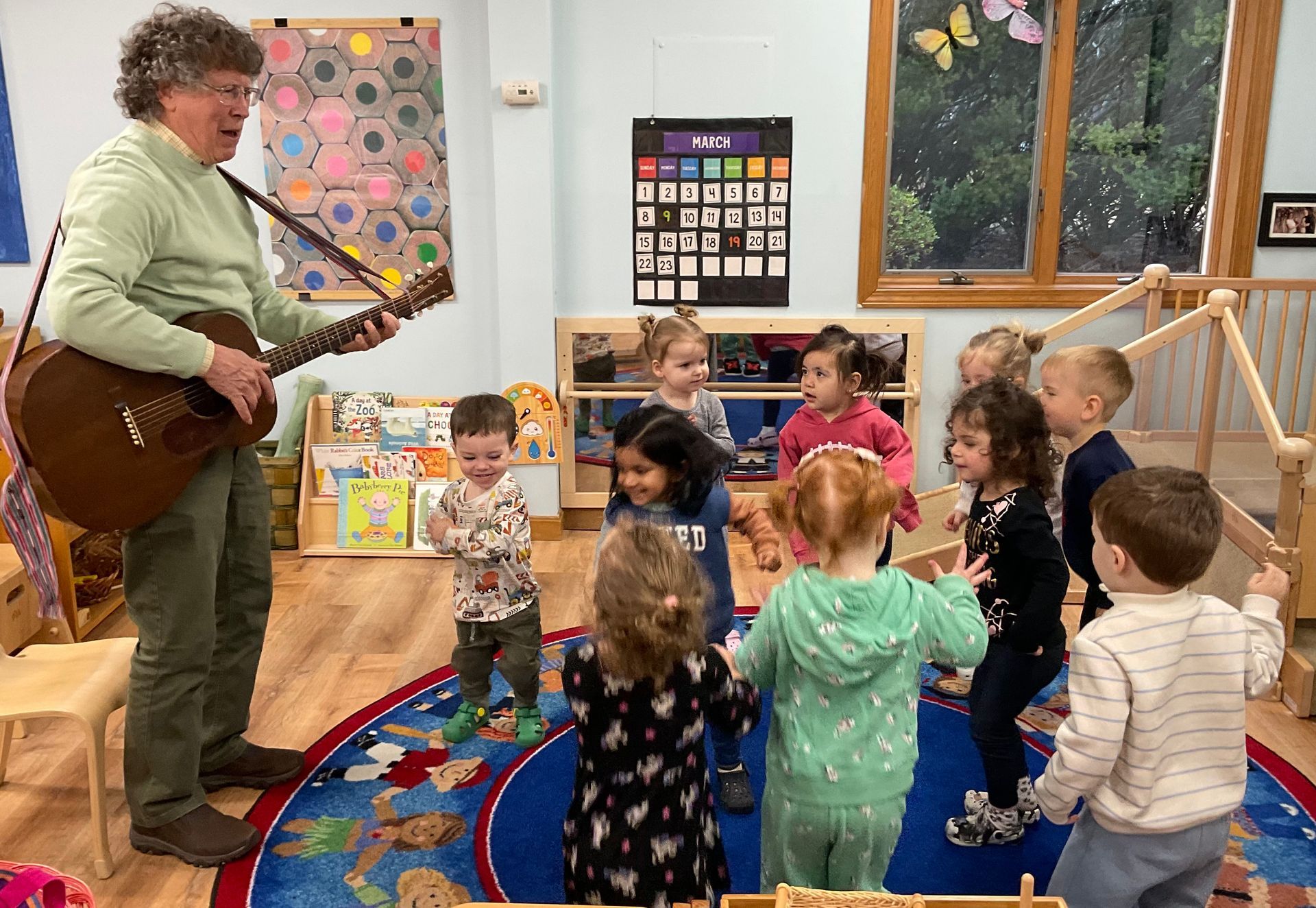 Musician playing guitar to a small group of children in a colorful classroom