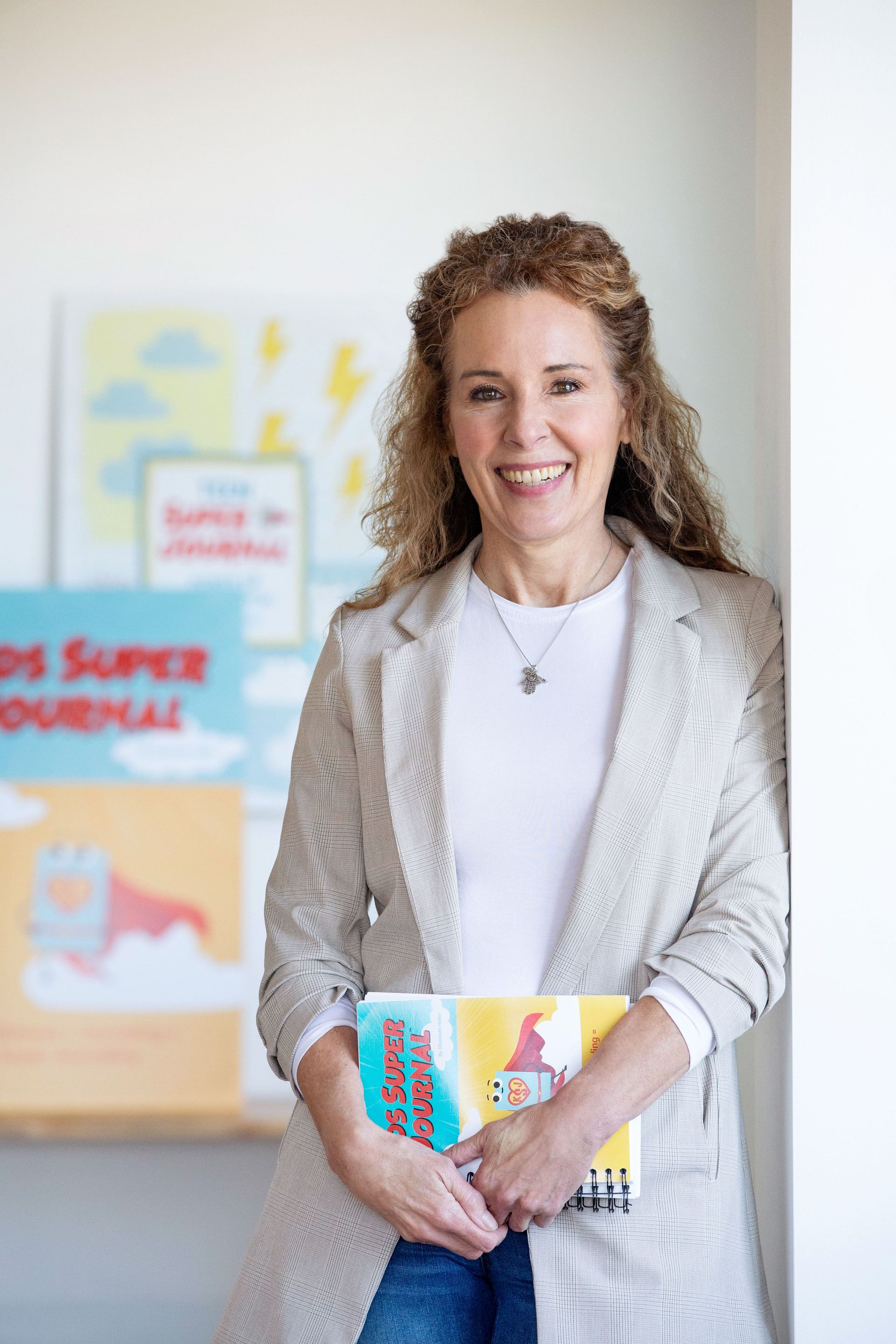 Montessori guide smiling, holding books, leaning against a wall; bright setting with book covers visible.