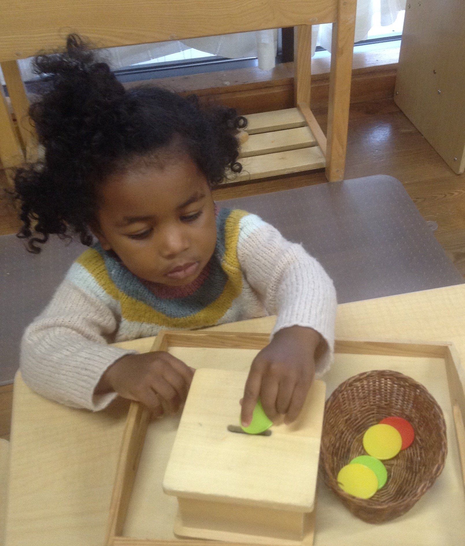 Montessori child playing with wooden shapes on a table, placing one in a slot.