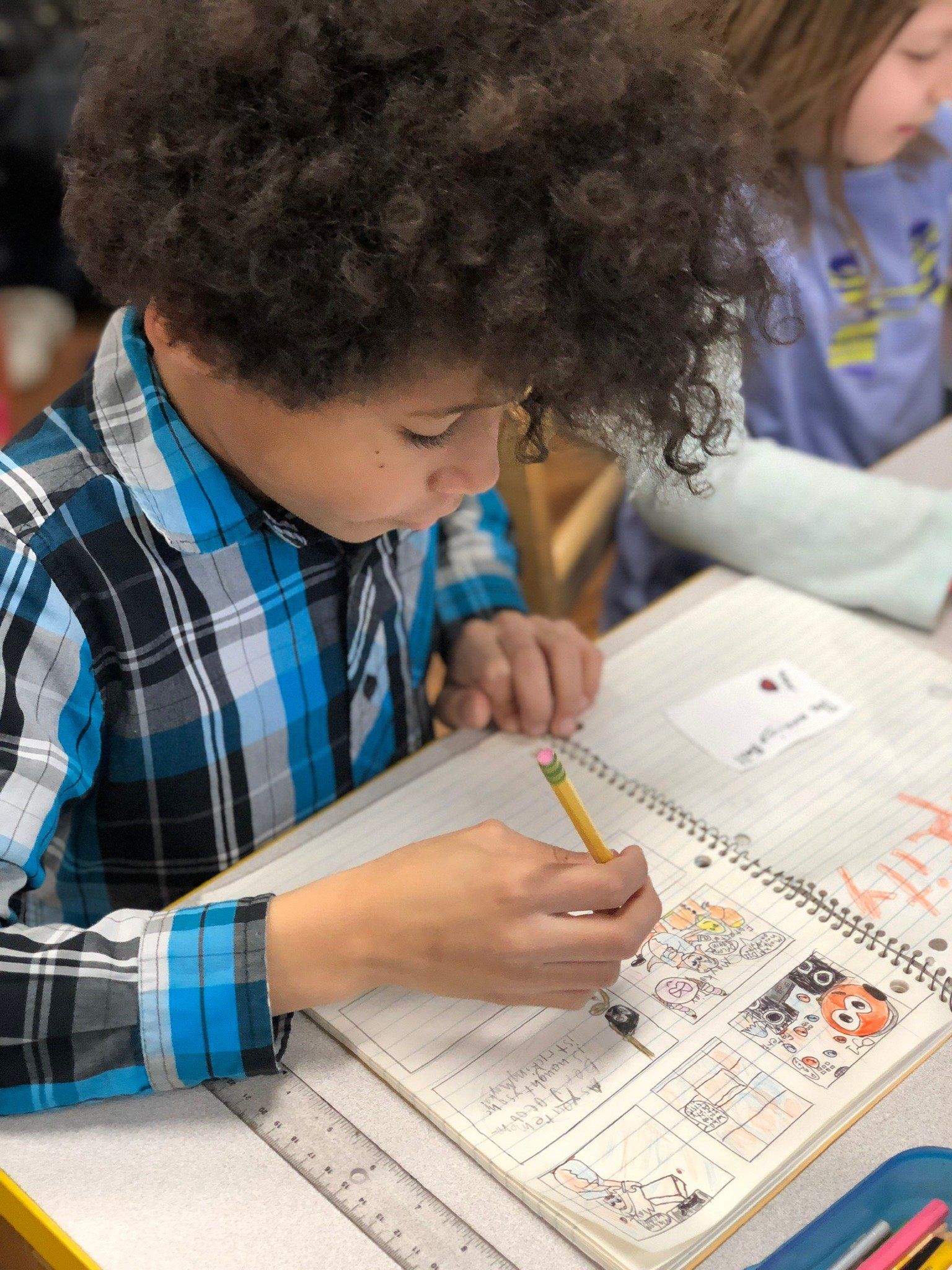 A young boy in a plaid shirt is writing in a notebook