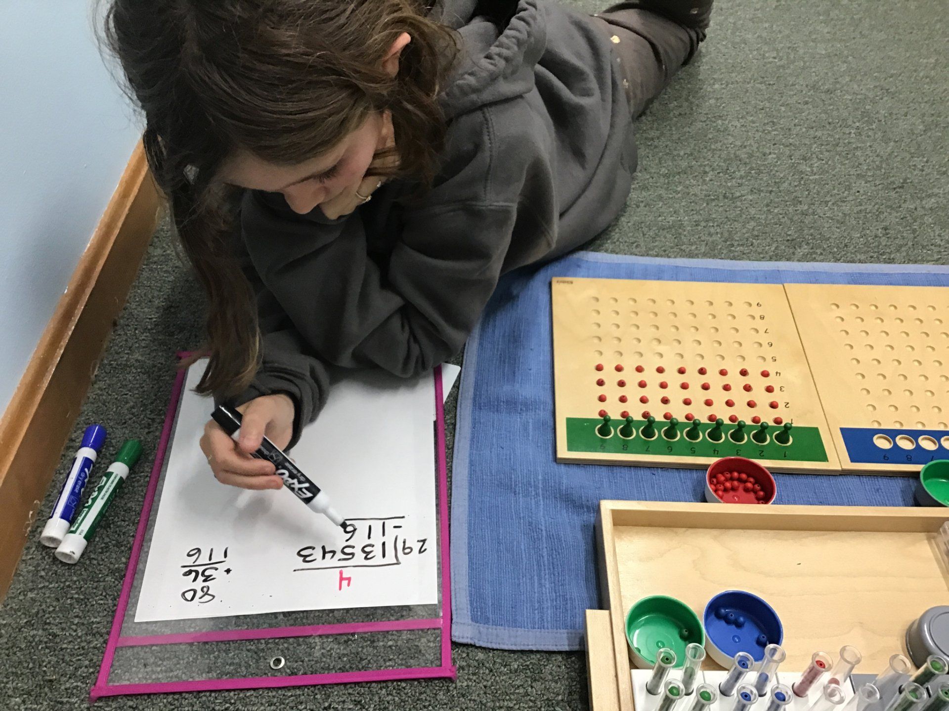 A young girl is laying on the floor with math montessori materials.