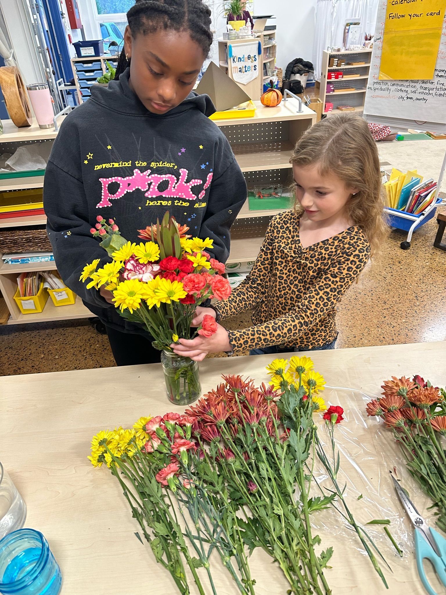 Two Montessori child are arranging flowers in a vase in the classroom.