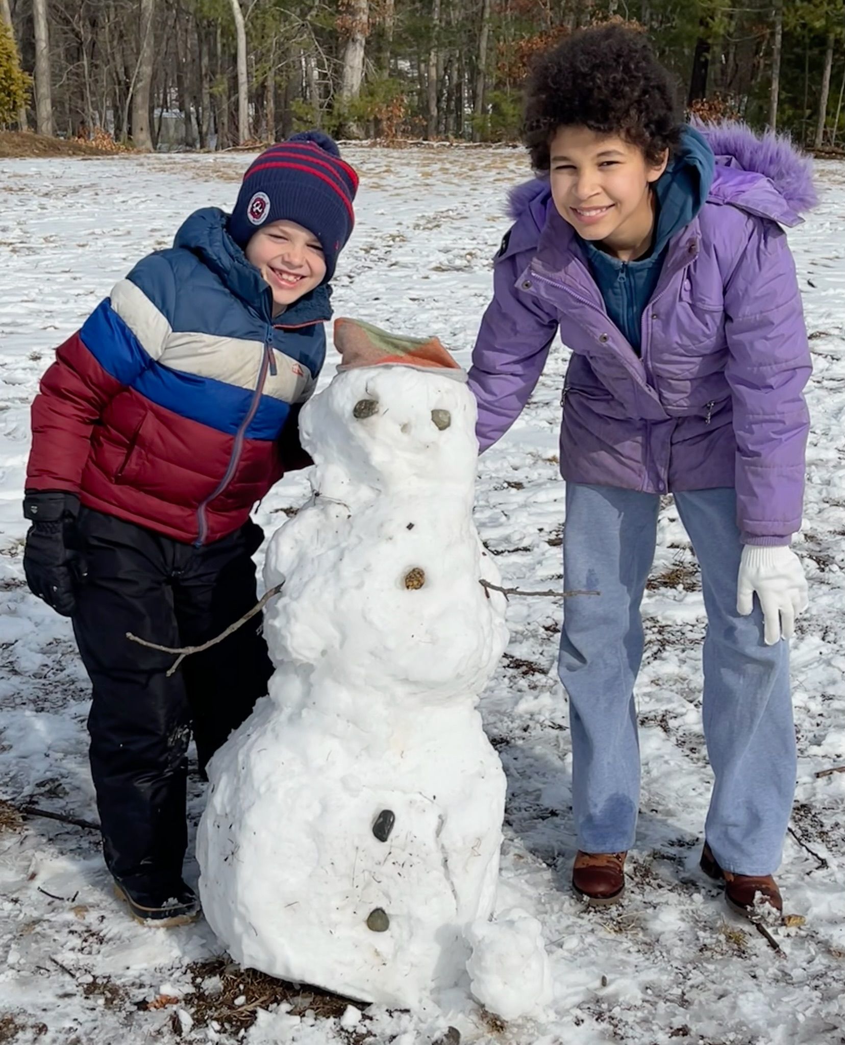 Two montessori chidrens are standing next to a snowman