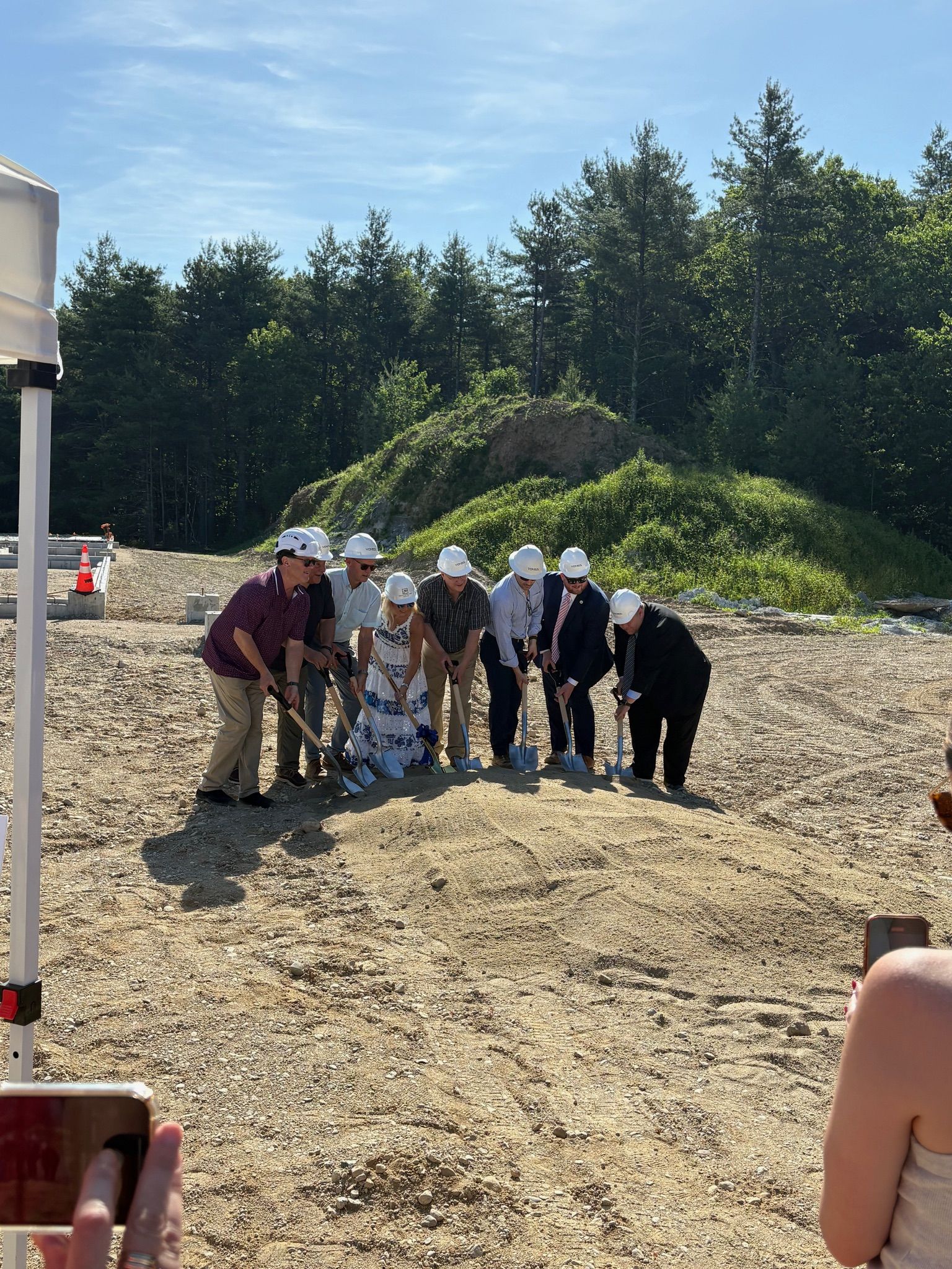 A group of people wearing hard hats and shovels are standing in a dirt field.