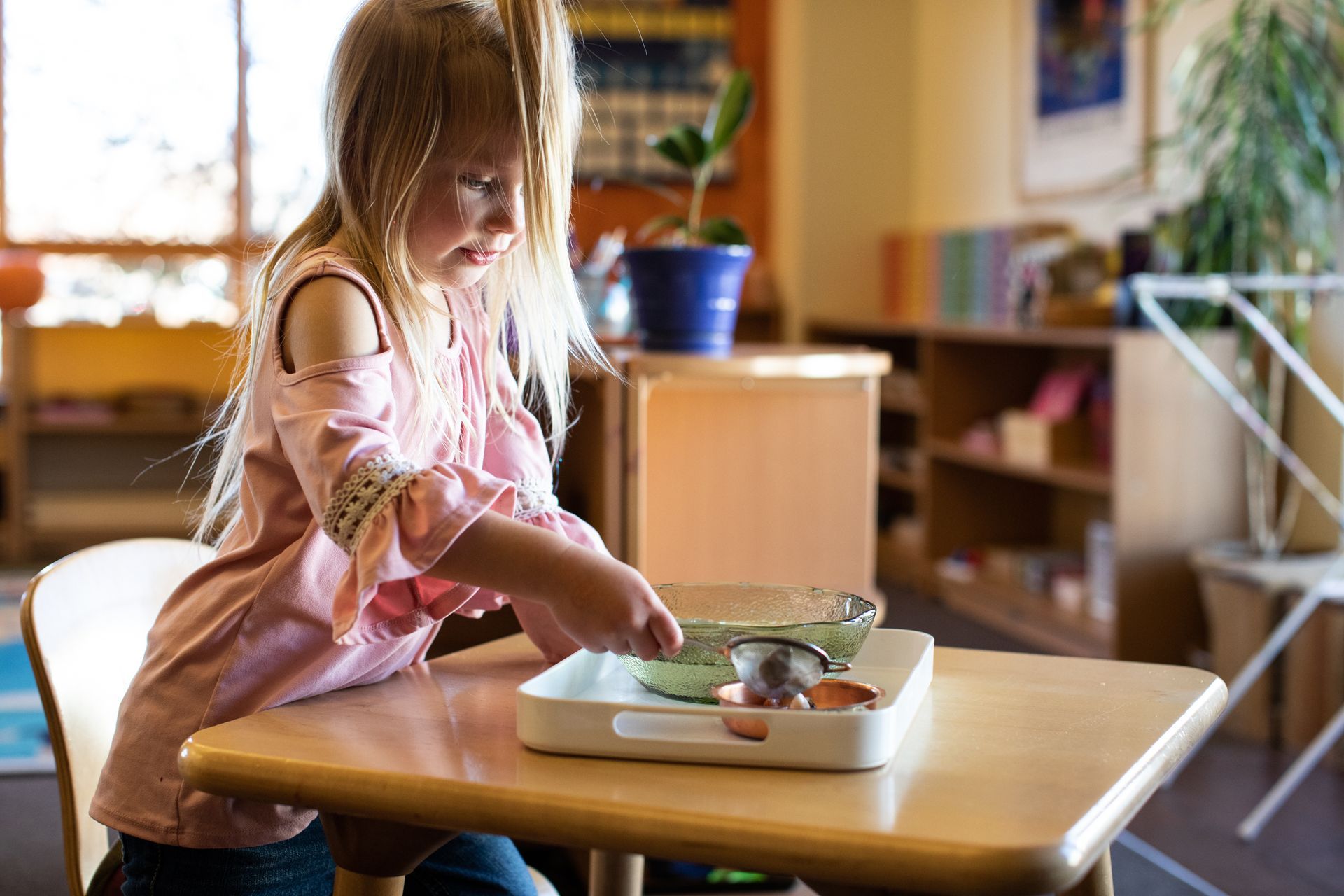 Montessori child focused on activity at a small table; indoor classroom setting.