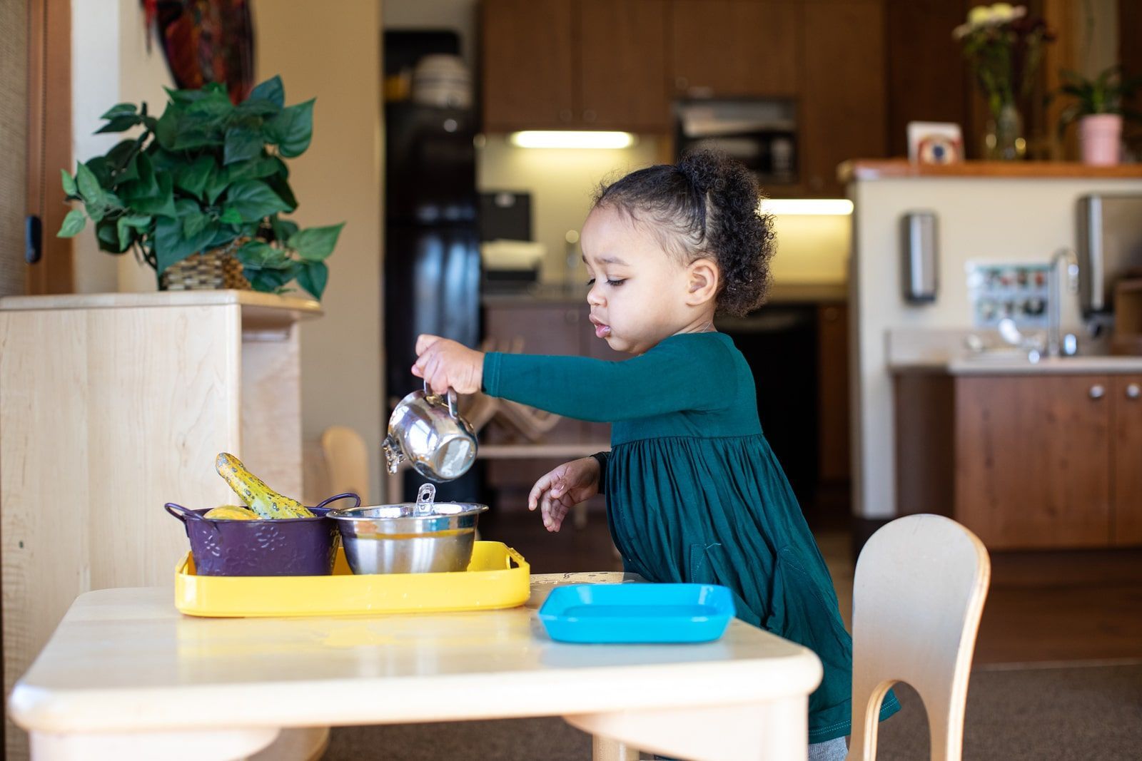Child pouring water from a silver pitcher into a bowl at a child-sized table.