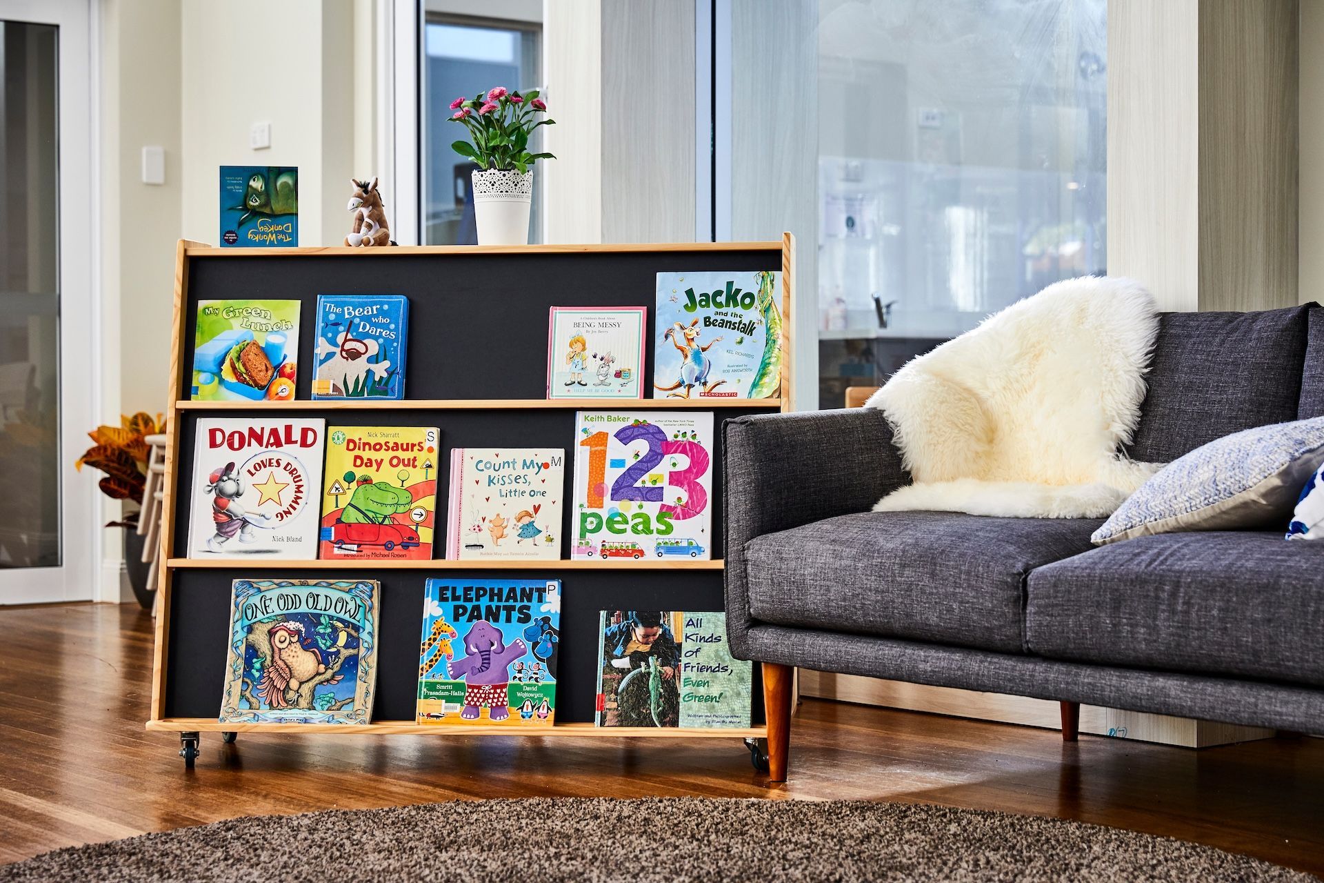 Bookshelves with children's books, a gray sofa, and a rug in a well-lit living room.
