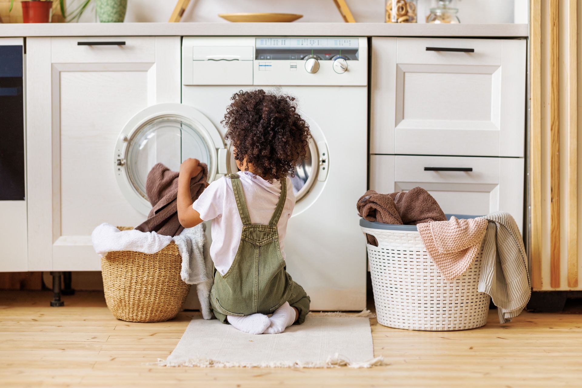 Montessori Child putting clothes in a washing machine in a laundry room, with laundry baskets.