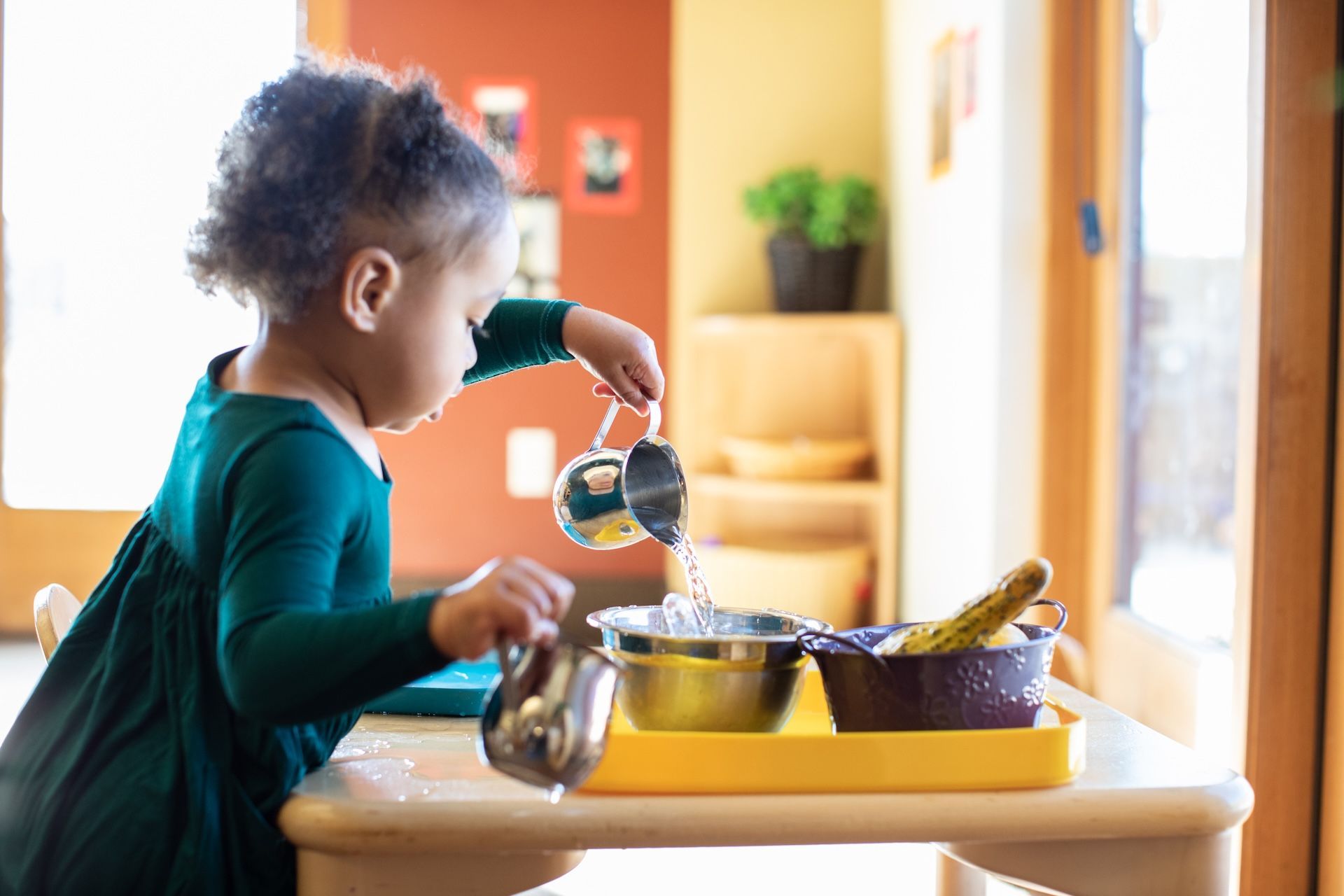 Montessori Child pouring water into a bowl at a table.
