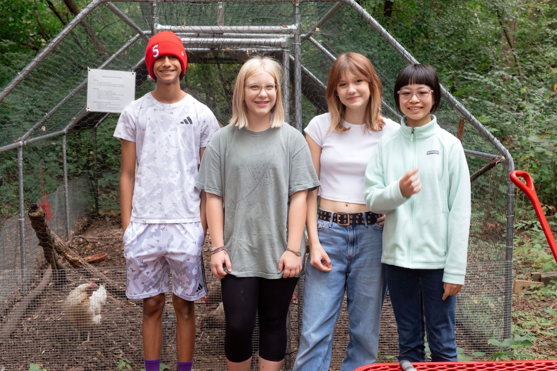 Montessori adolescents pose in front of a wire enclosure in a wooded area.