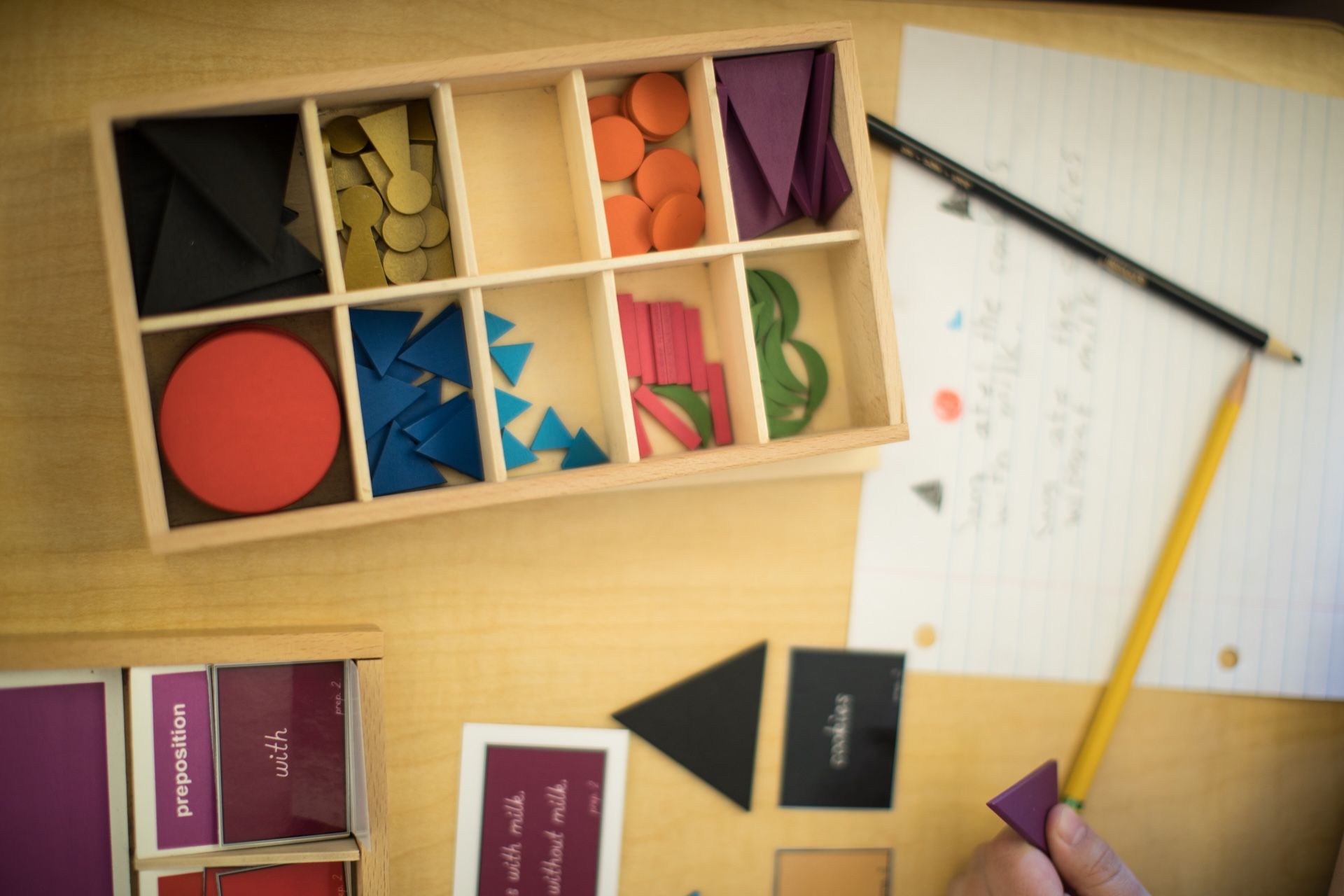 Wooden tray with geometric shapes, paper, and pencil on a table.
