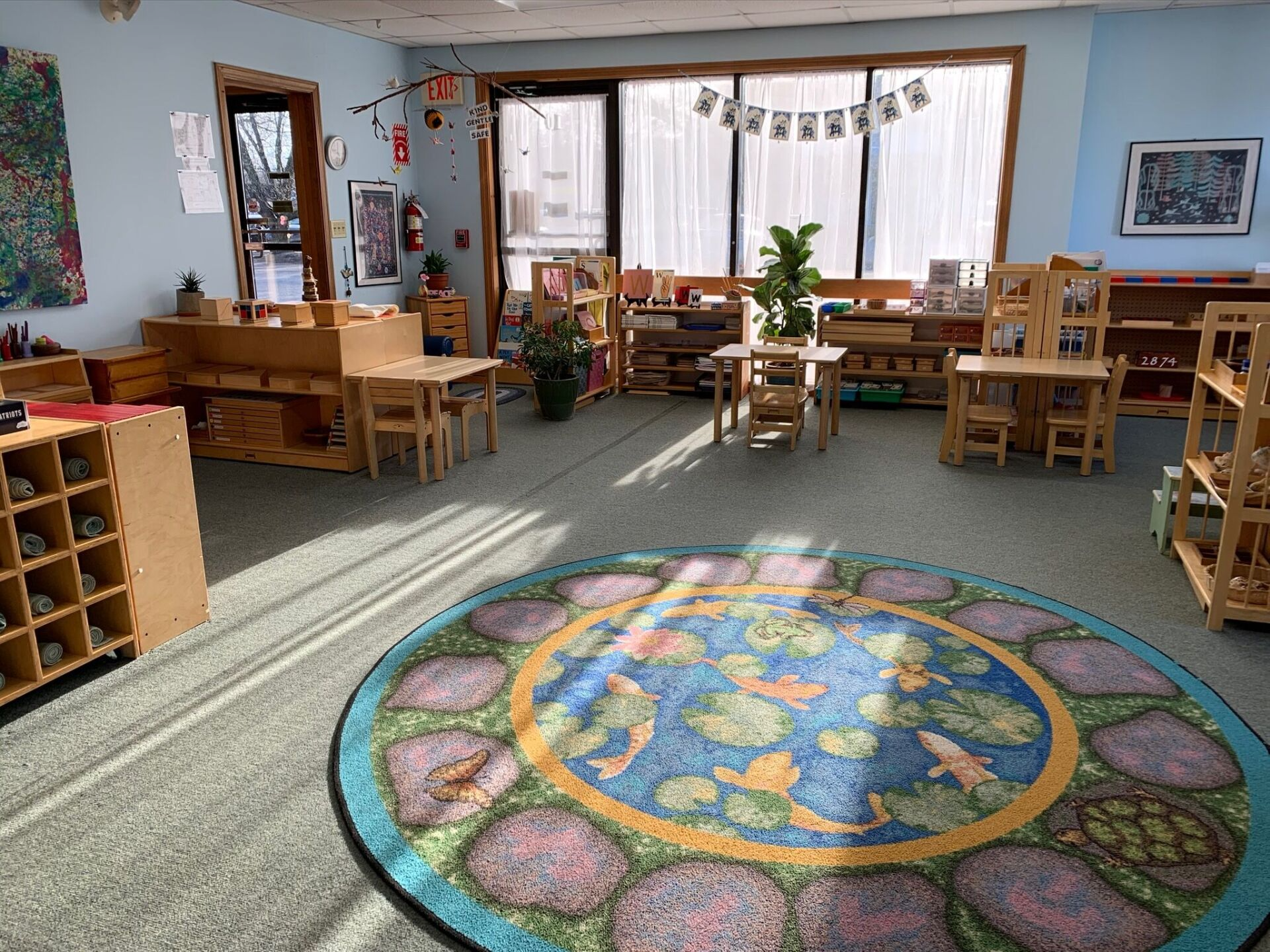 A montessori style classroom with tables and chairs and a rug on the floor.