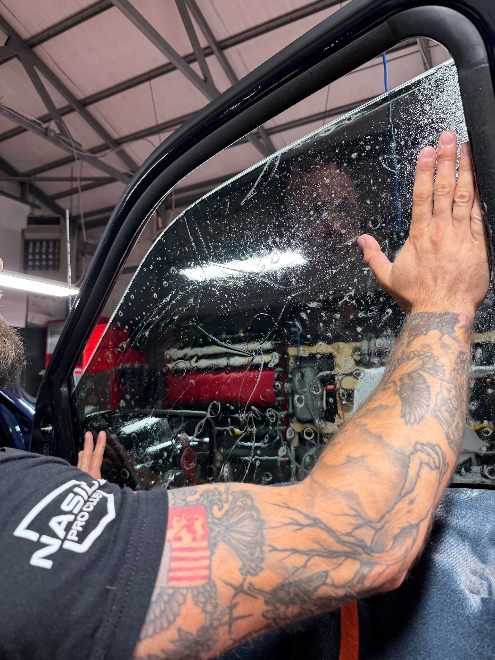Person applying window film to a dark blue car in a workshop