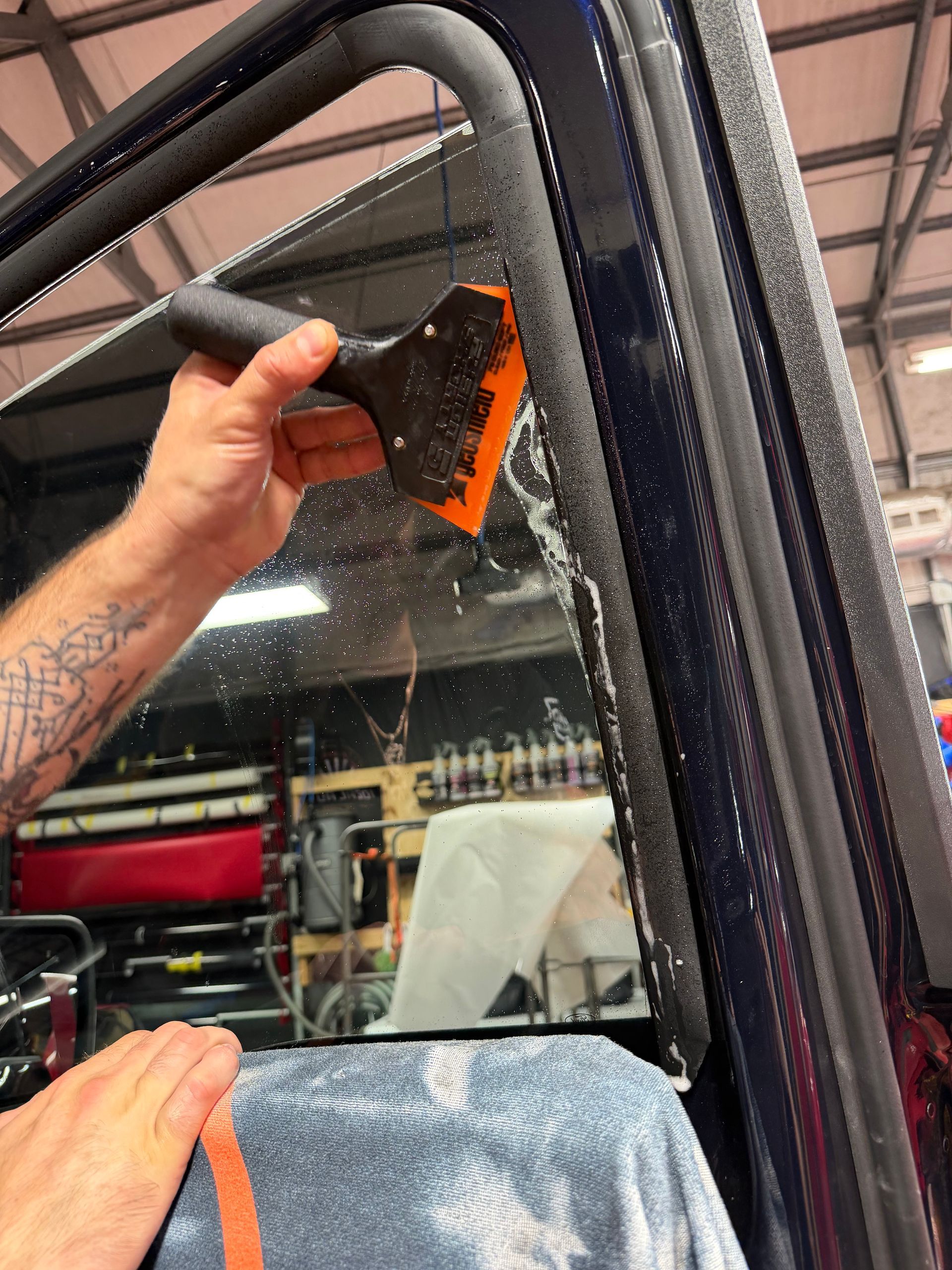 Person cleaning a large vehicle window with a squeegee inside a workshop