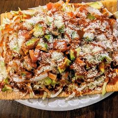 A loaded tostada topped with shredded meat, avocado, salsa, and grated cheese on a plate