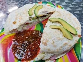 Two avocado-topped sandwiches with red salsa on a colorful plate