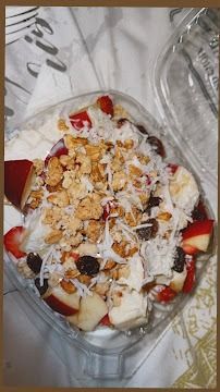 A glass bowl of yogurt topped with strawberries, granola, raisins, and cereal on a table.
